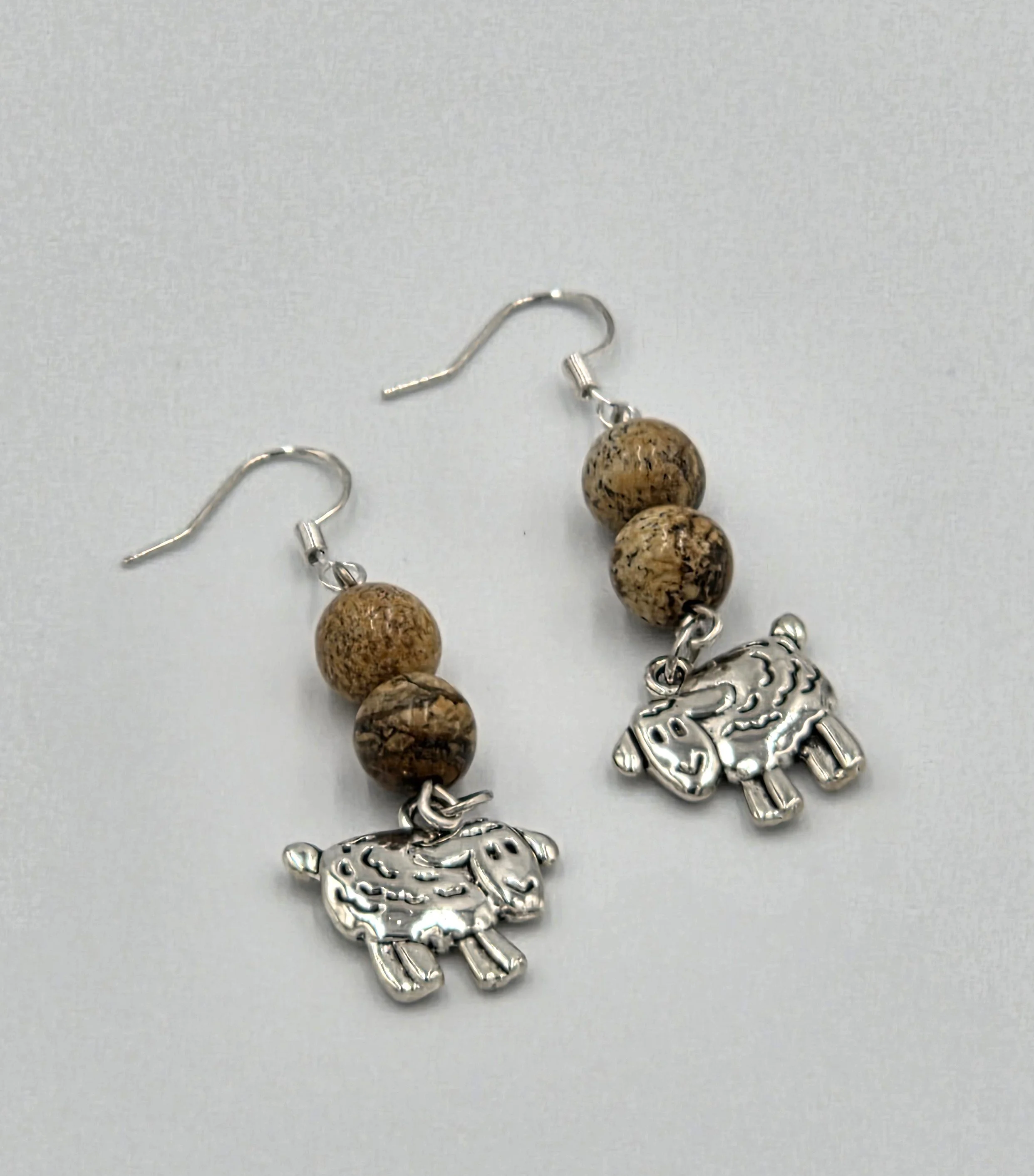 Silver sheep earrings with light brown patterned stone beads on silver hooks.