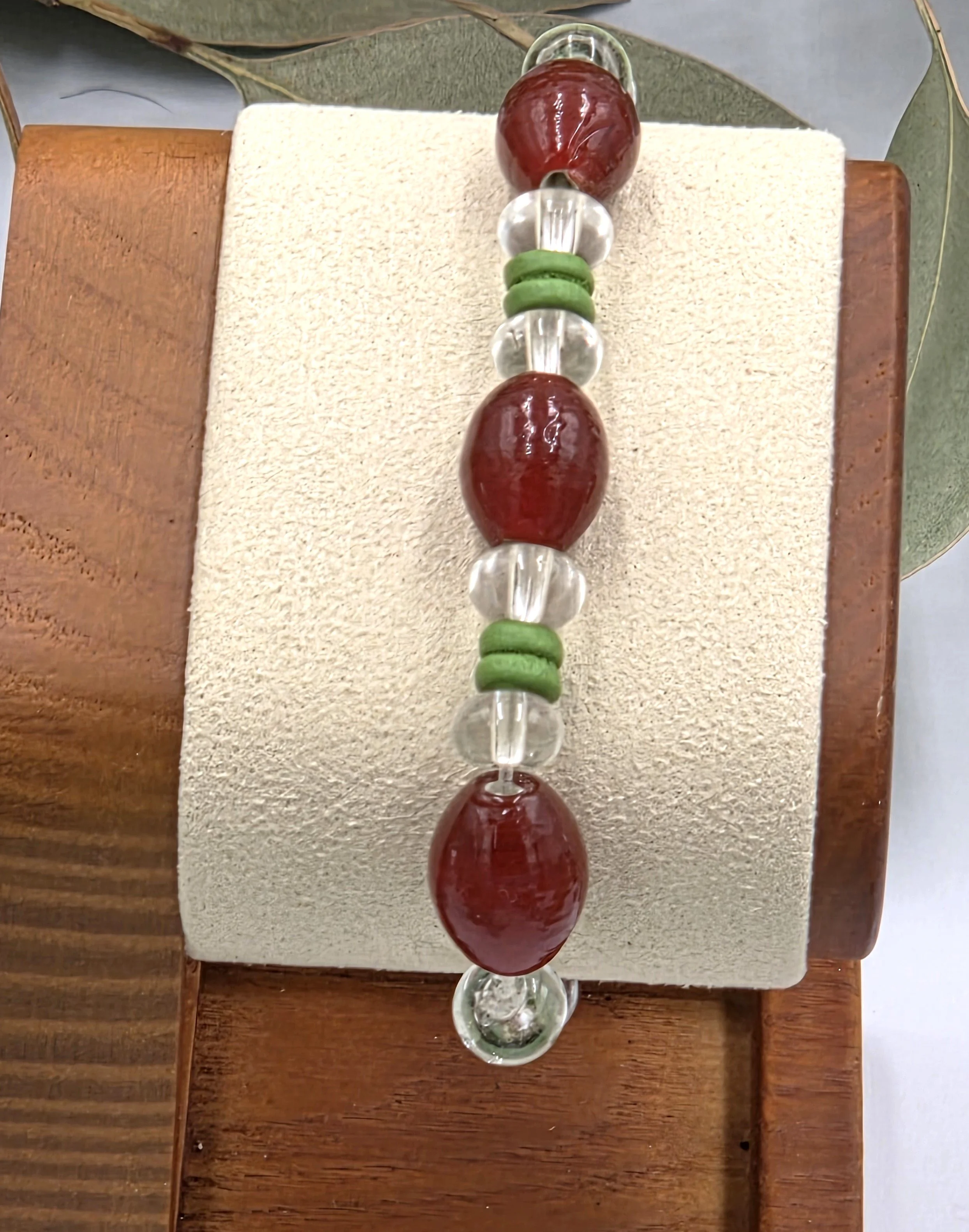 Rust red glass oval beads separated by clear glass donuts and forest green ribbed wood beads on an elastic bracelet.