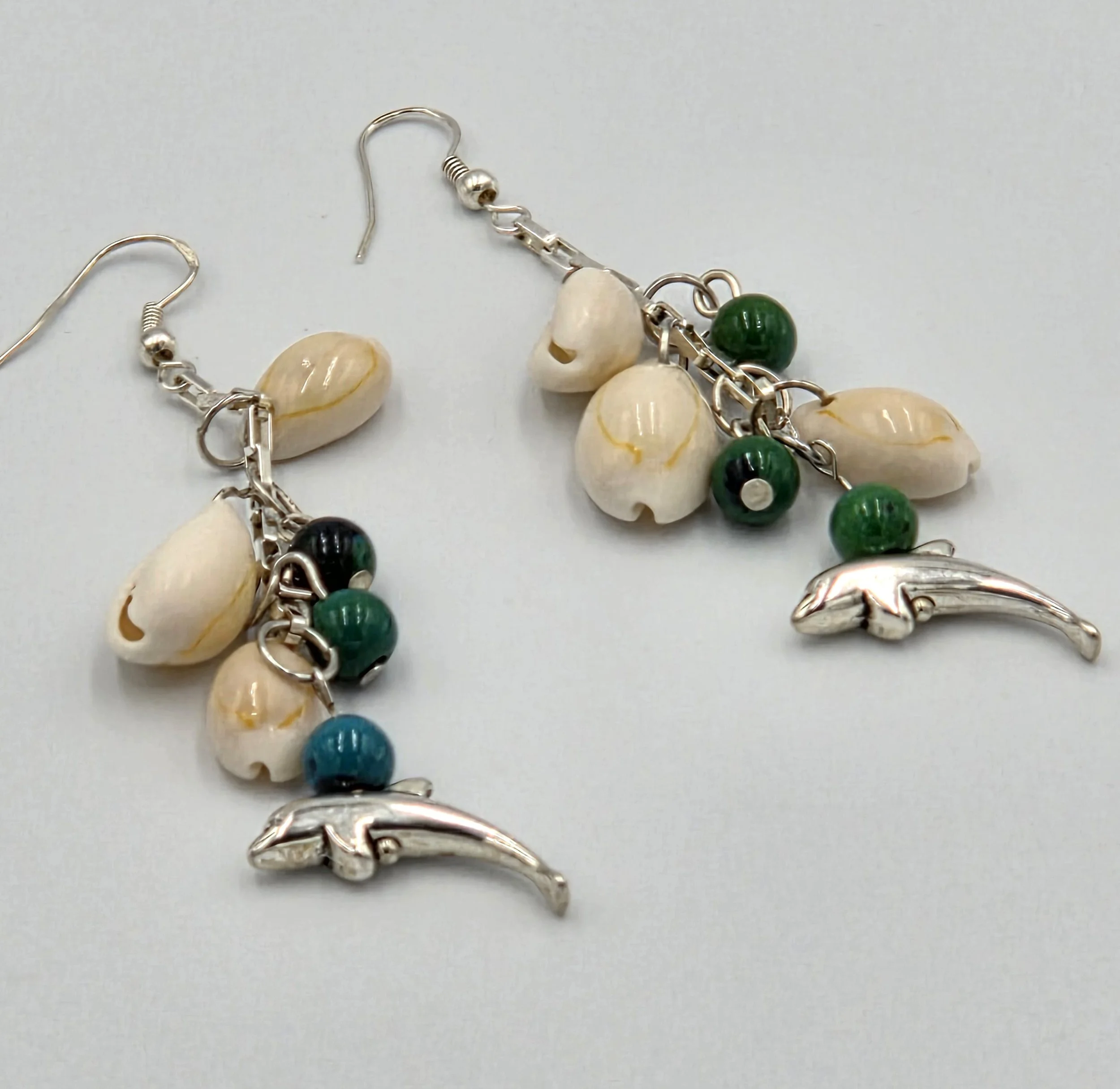 Long silver chain earrings with three cowrie shells, three blue-green gemstones, and dolphin charms.