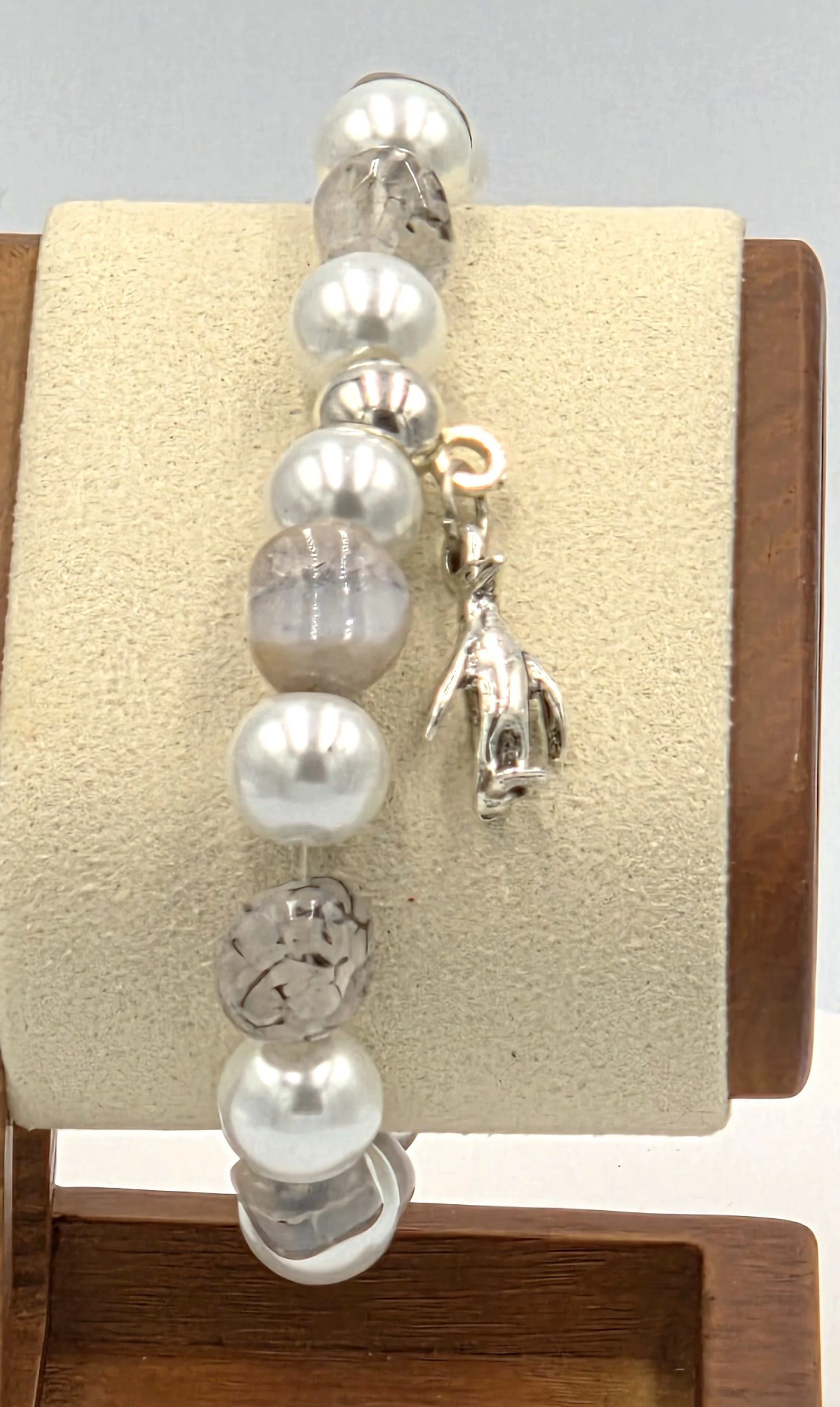 close up of OOAK white pearl and translucent brown agate bracelet with silver penguin charm.