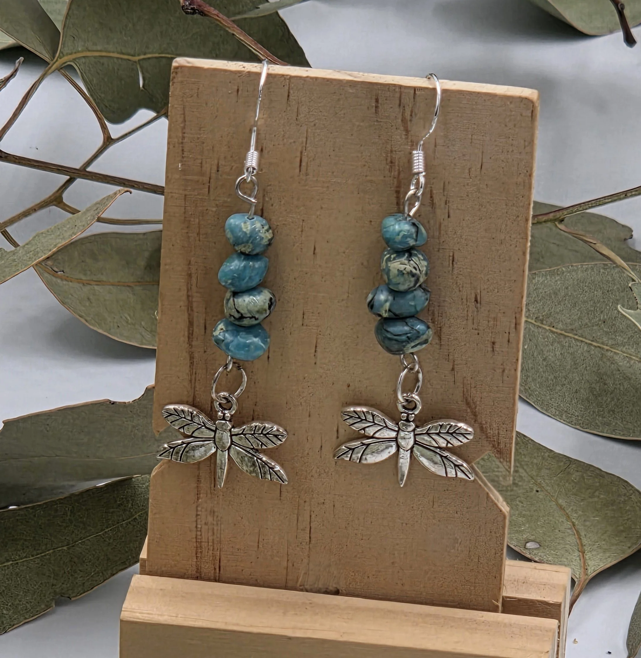 Dangle earrings with stacked turquoise nuggets and a silver dragonfly charm on sterling silver hooks.