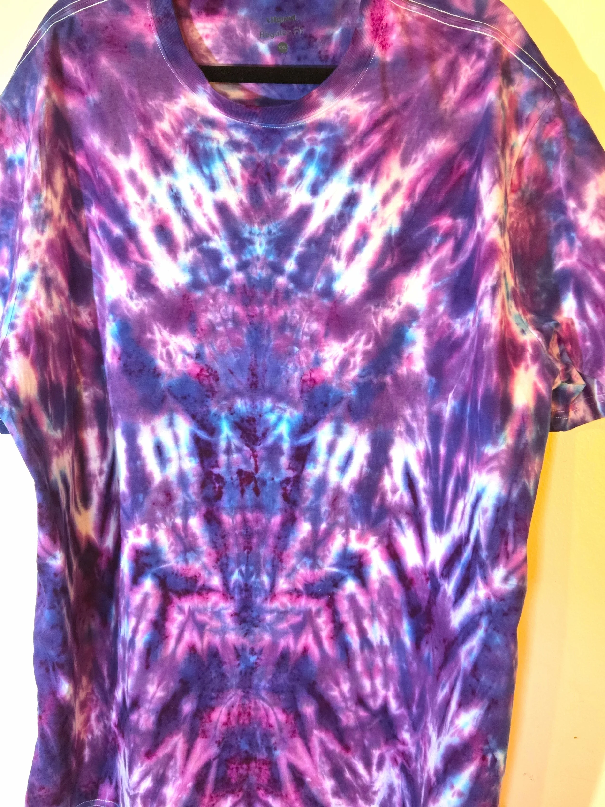 An adult XXL t-shirt featuring an intense red and burgundy tie-dye pattern that shapes a narrow fan at the neck and expands into a horizontal psychedelic design near the hem.