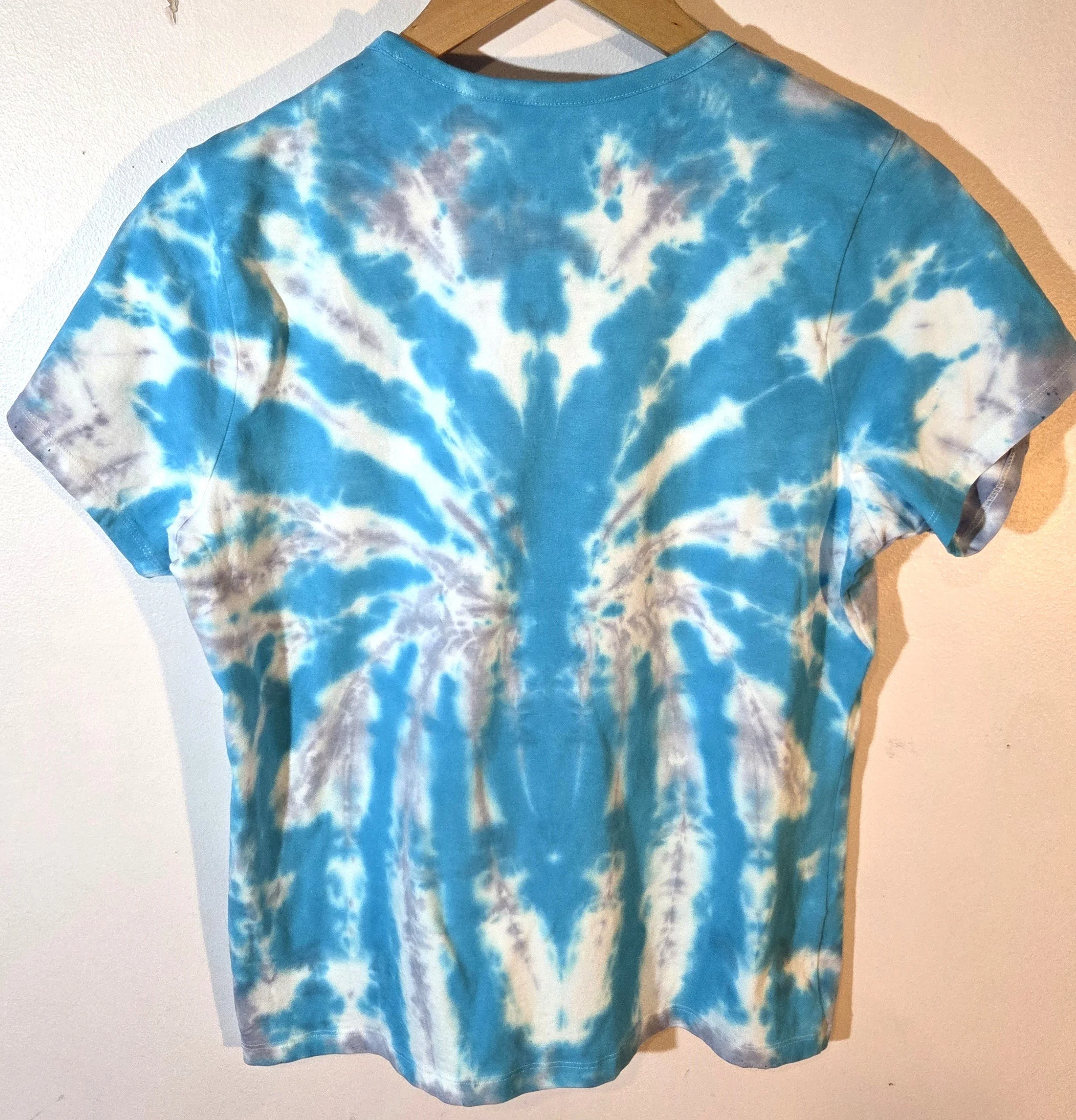 back view A size 16 t-shirt featuring a highly defined tie-dye spider pattern in bright aquamarine against a soft grey and white background.
