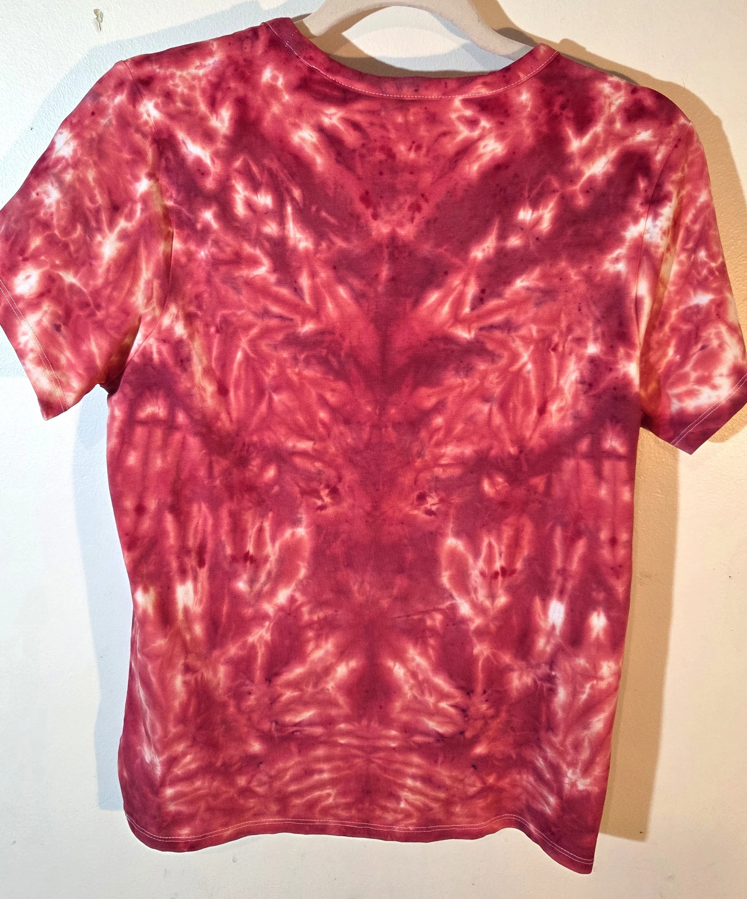 back view of A size 14 women's t-shirt featuring a highly saturated red and coral tie-dye pattern of abstract swirls radiating from the center.