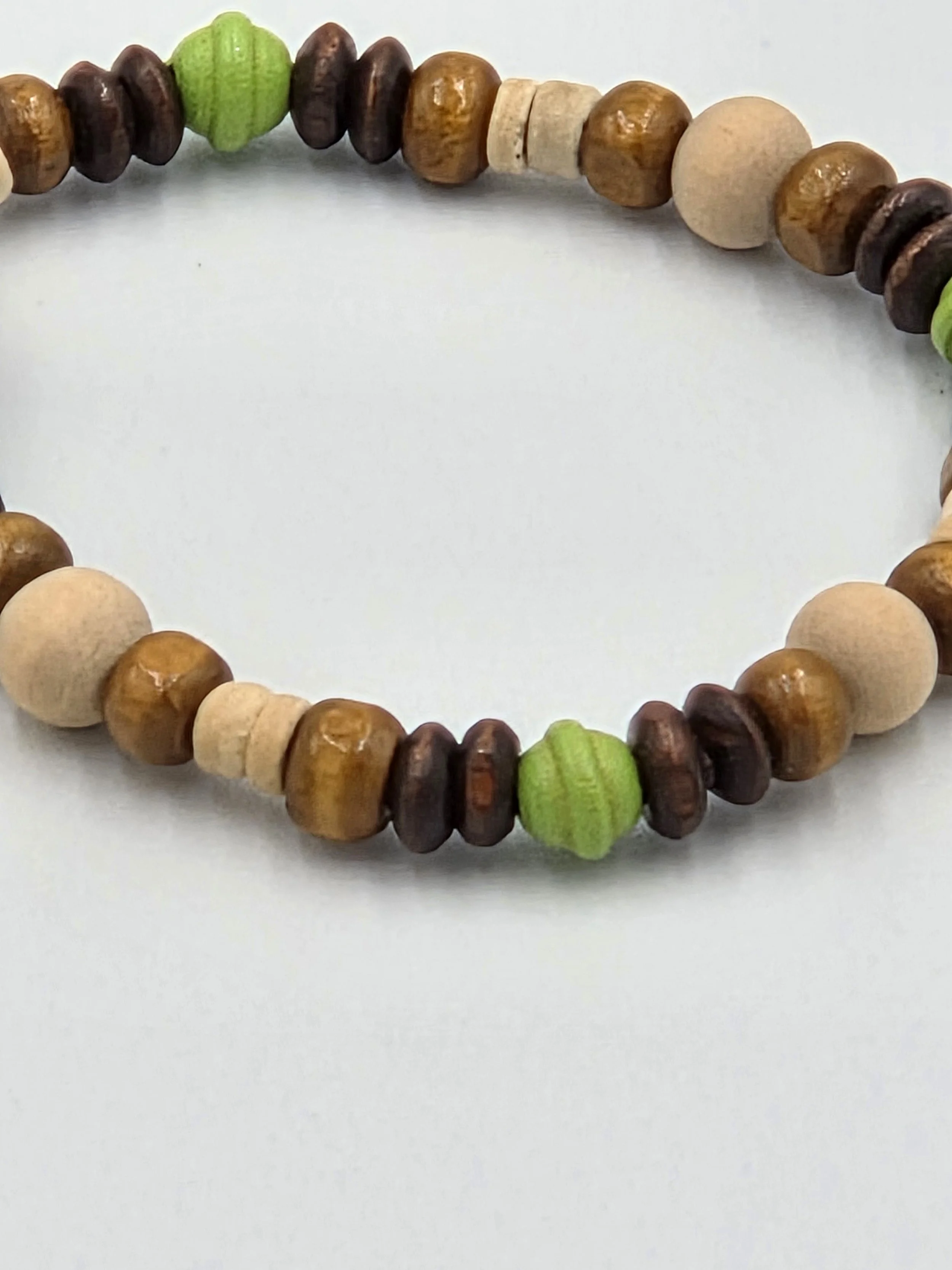 Small elastic bracelet with cream, brown, and lime green wooden beads in varied shapes.