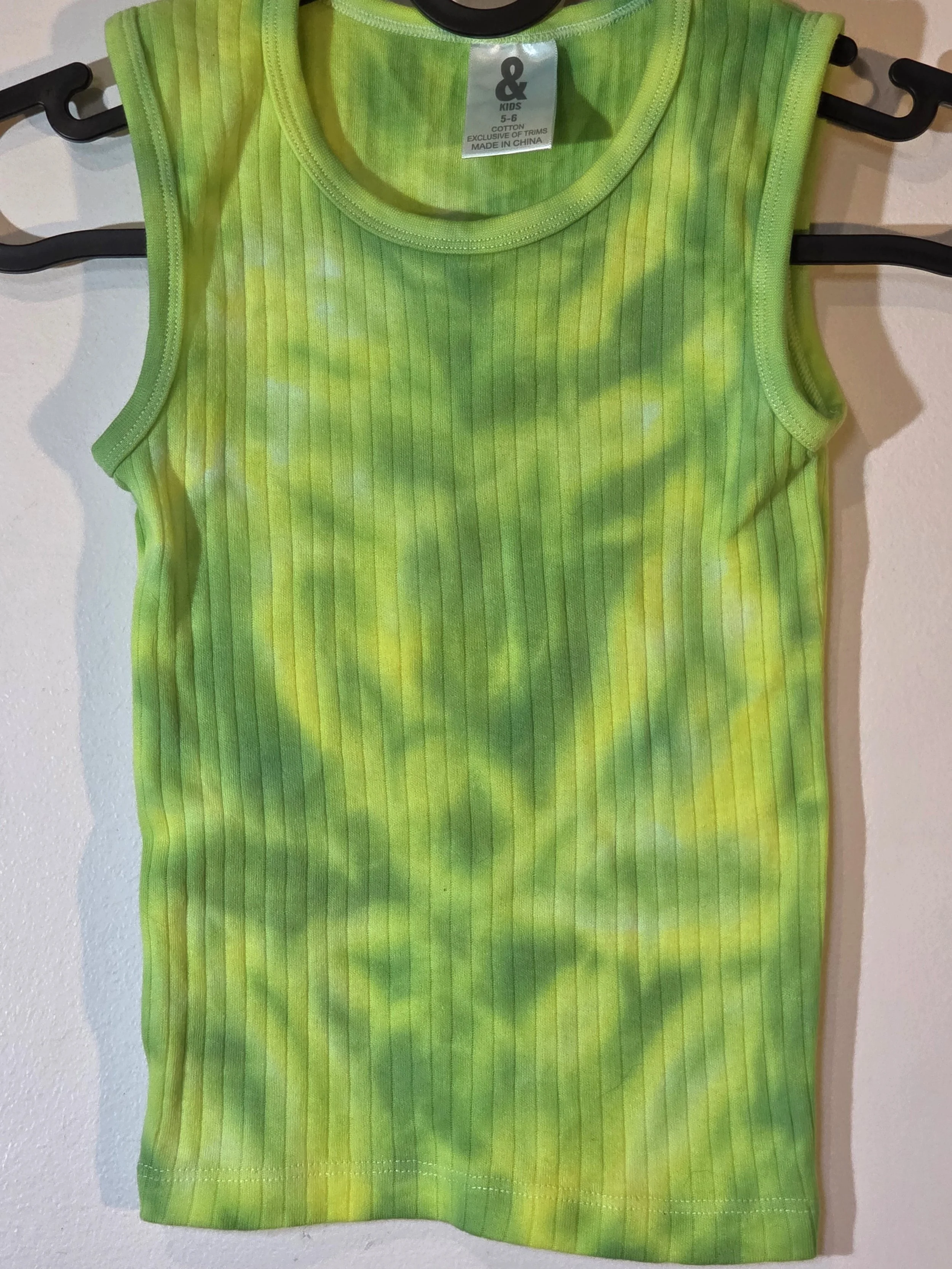 close up of A child's ribbed singlet featuring a faint, pastel tie-dye pattern of lime green and yellow that creates a soft abstract flower shape near the bottom hem.