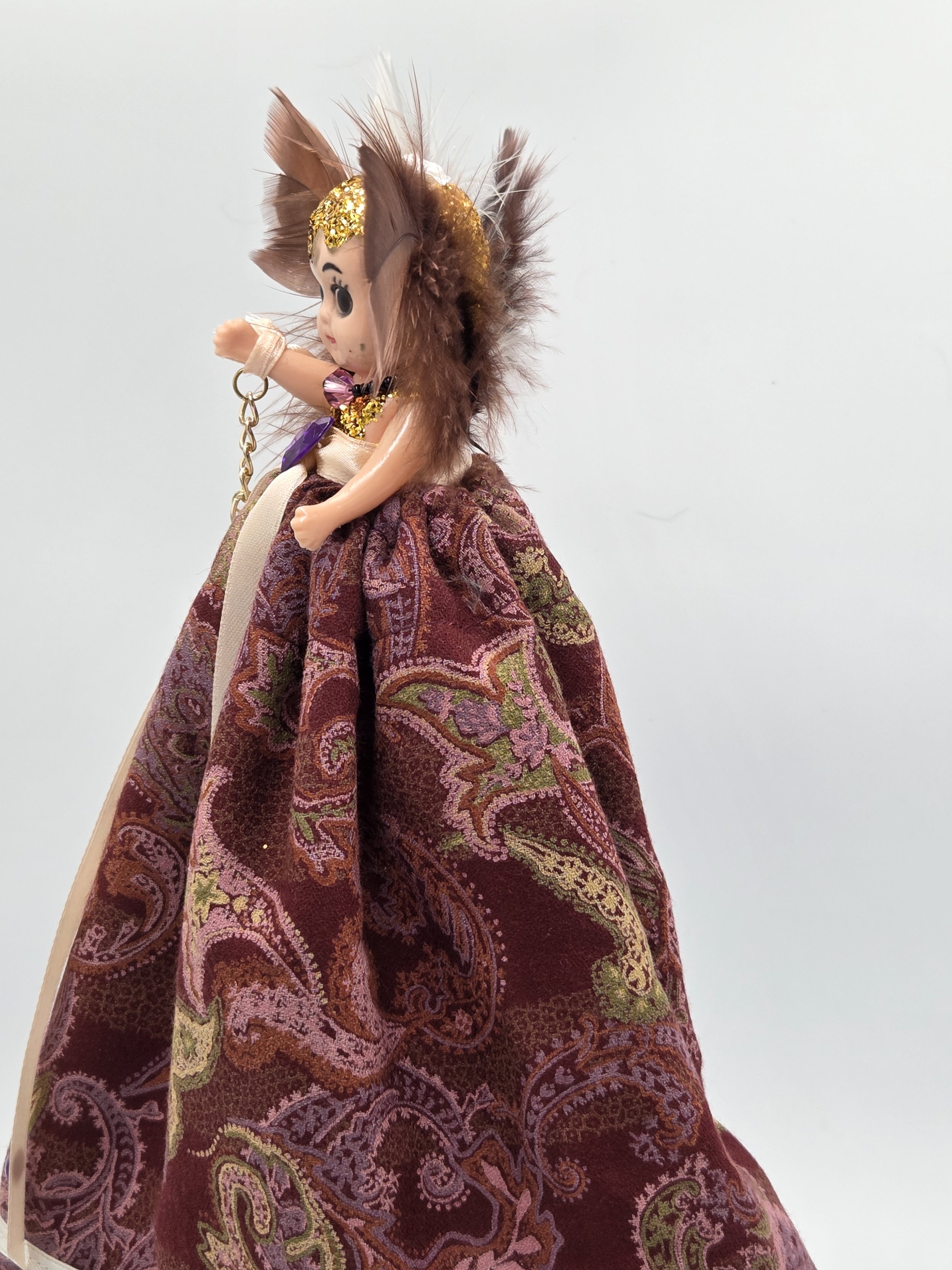 close-up side view of Isadora Art Doll in burgundy paisley gown with white lace and feather surround.
