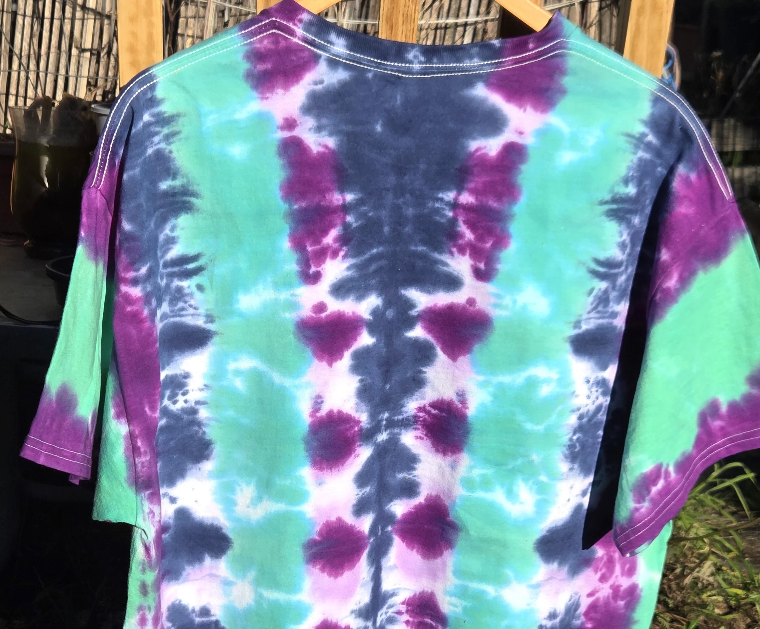 back view of An adult size XL cotton t-shirt featuring vertical tie-dye columns in dark blue, purple, soft lilac, and solid teal green.