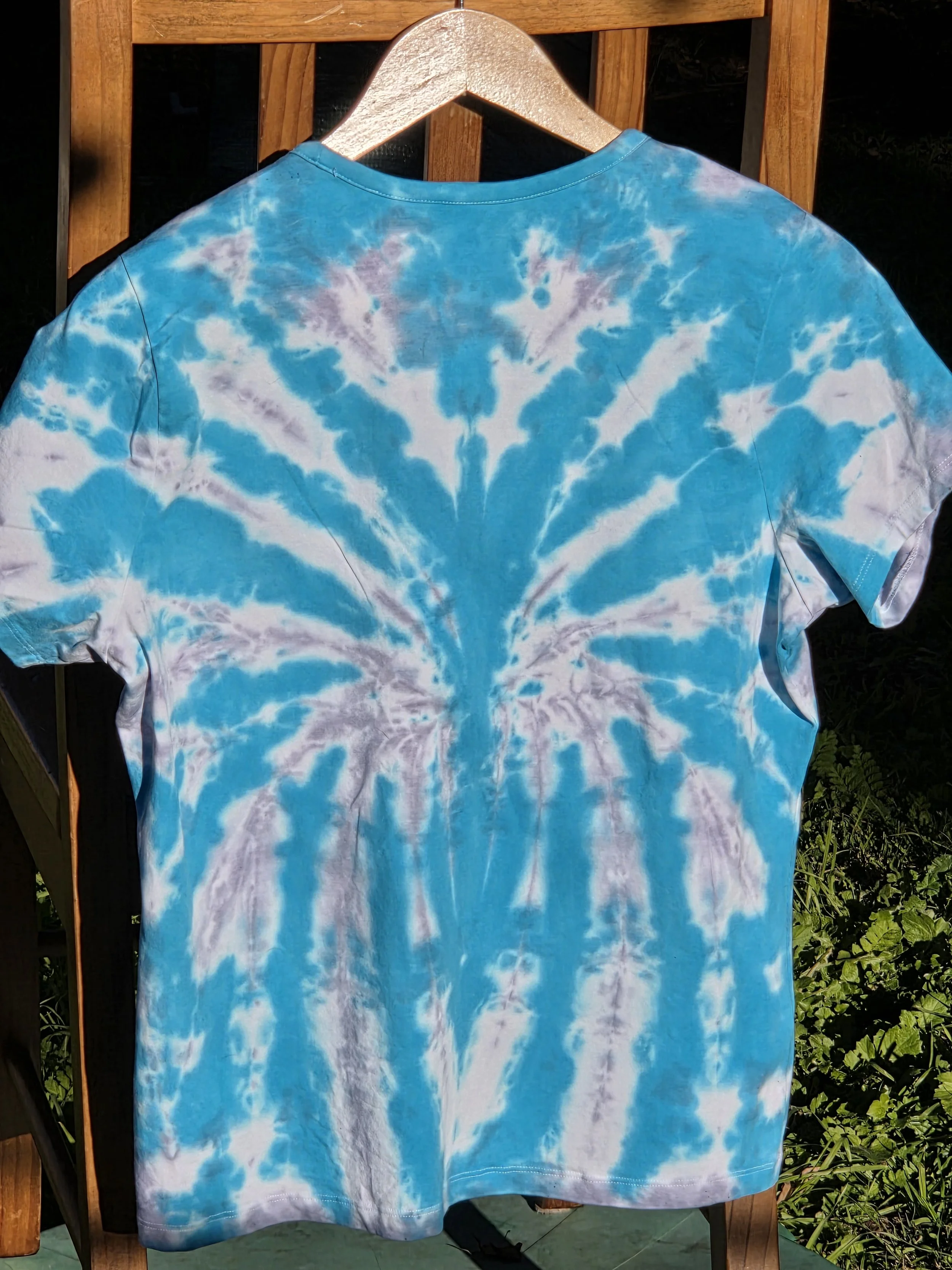 back view of A size 16 t-shirt featuring a highly defined tie-dye spider pattern in bright aquamarine against a soft grey and white background.
