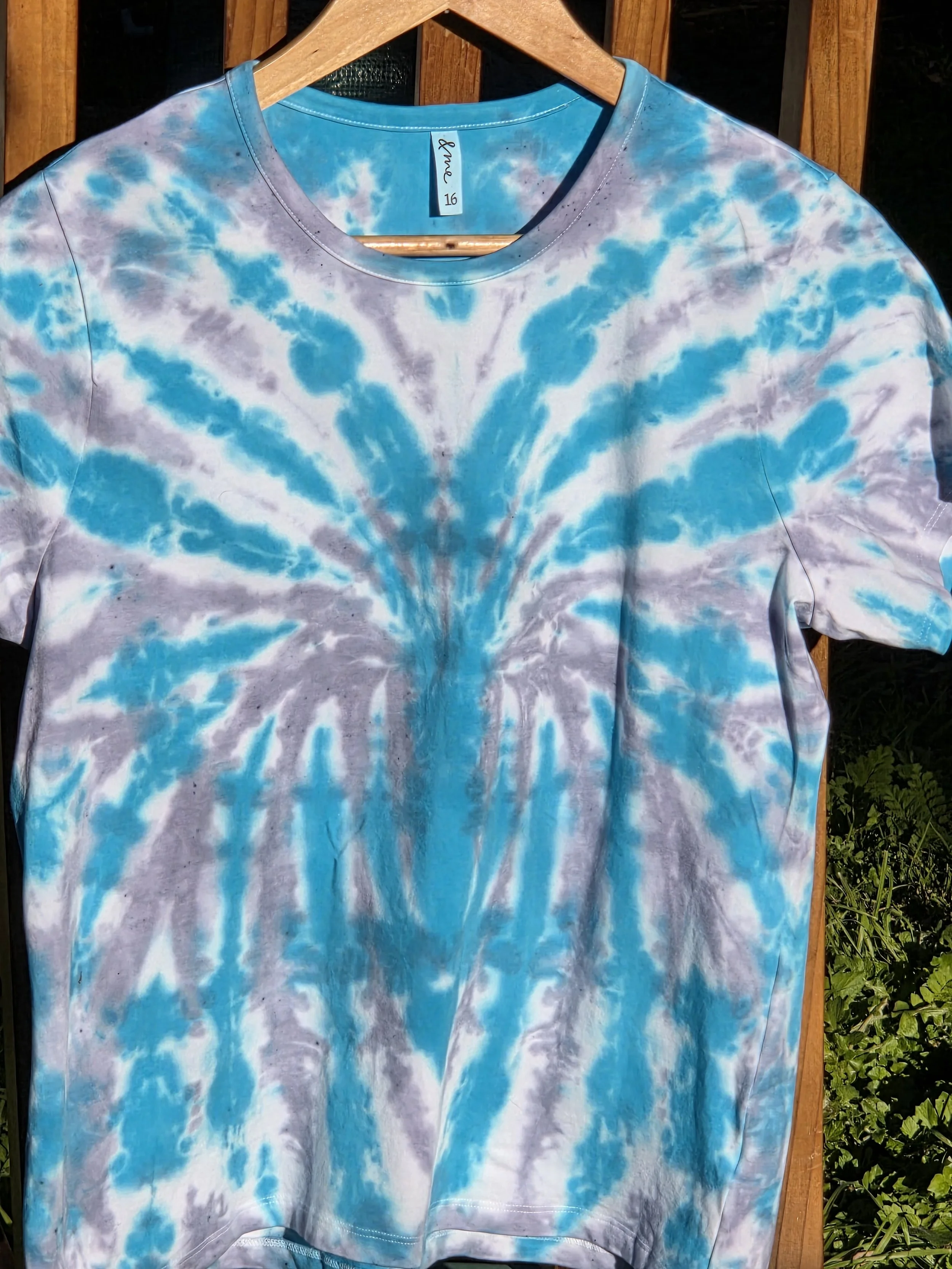 A size 16 t-shirt featuring a highly defined tie-dye spider pattern in bright aquamarine against a soft grey and white background.
