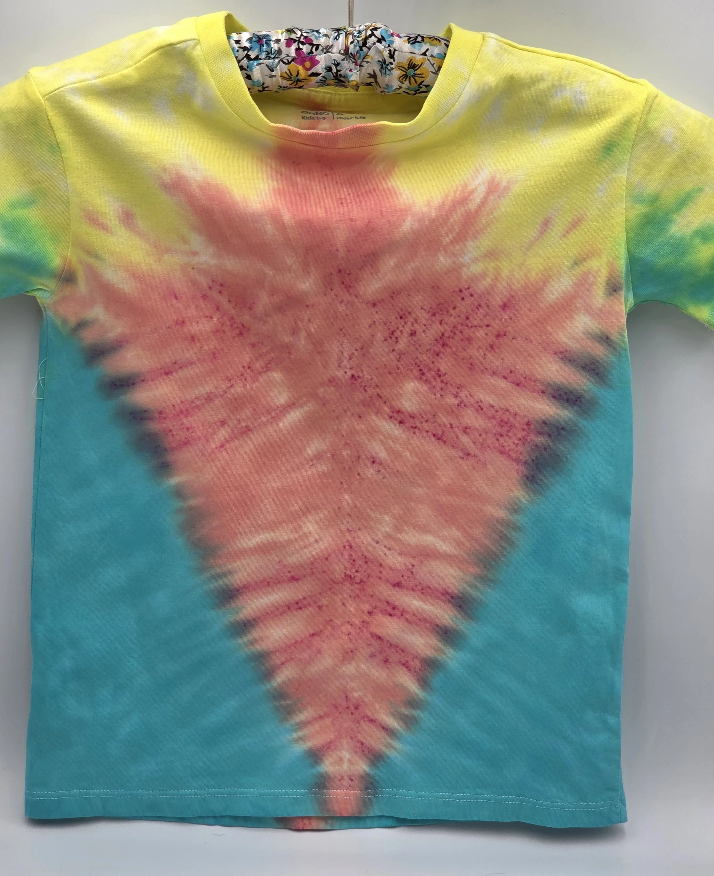A child's size 6 t-shirt with a half Y-fold tie-dye pattern featuring a central coral V-shape framed by teal sides and yellow shoulders.