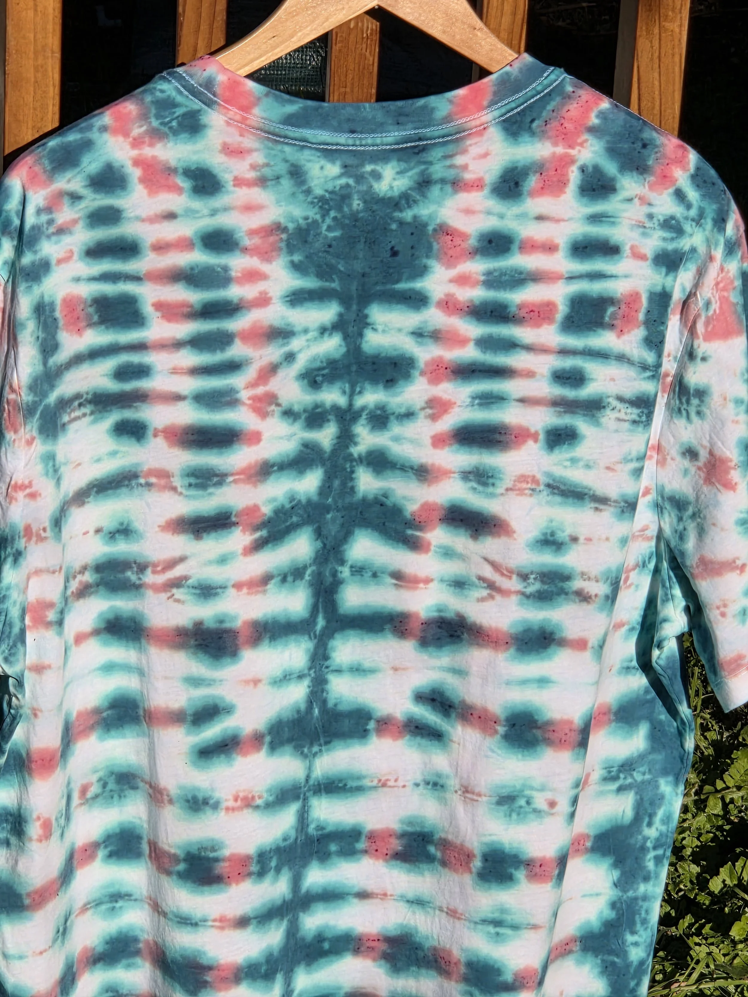 back view of An XL adult white t-shirt featuring a tie-dye grid of Aegean green and coral with a prominent green centerline and eye motif near the neck.