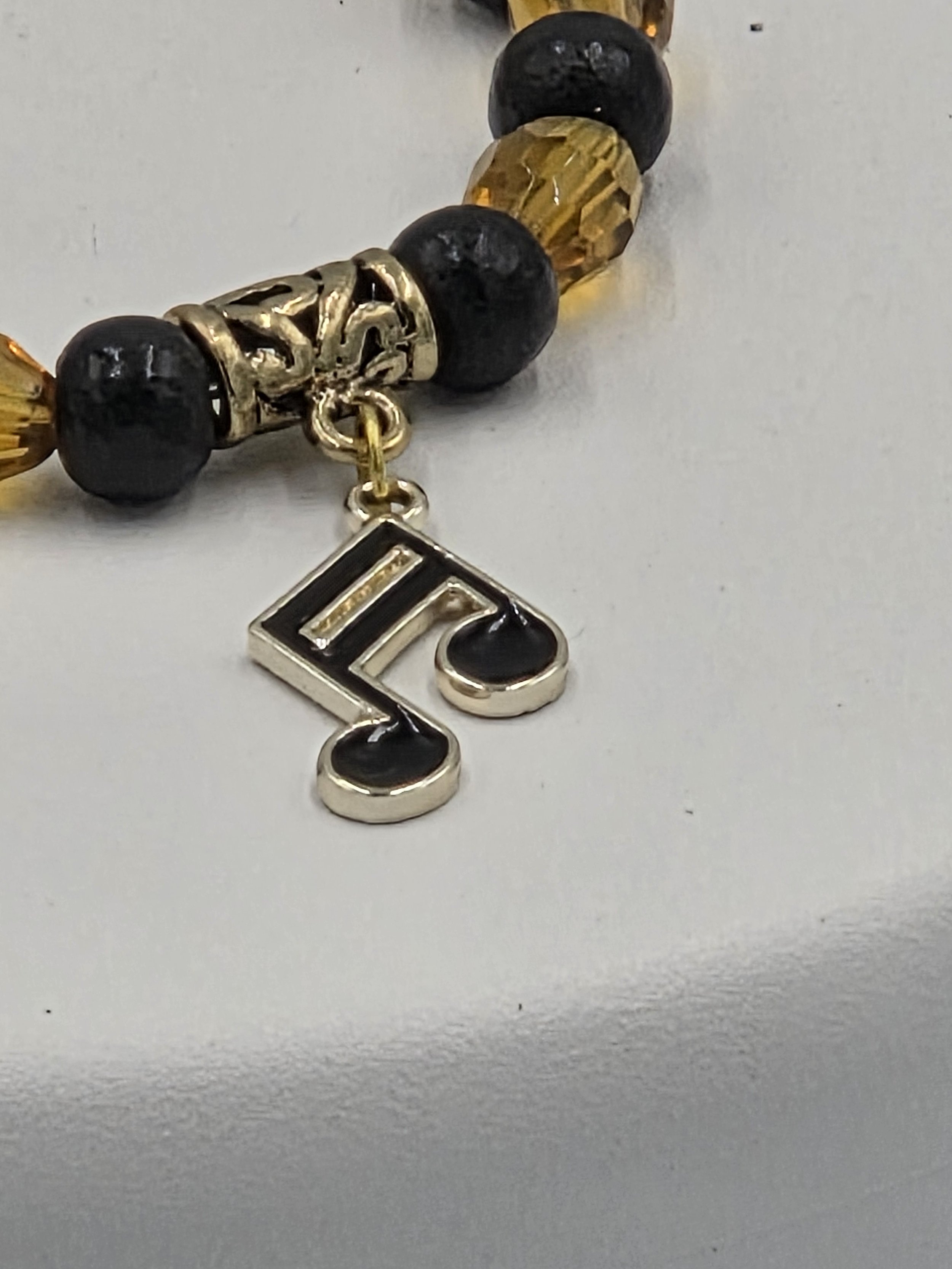 close up of OOAK amber glass and black wood bracelet with gold & black musical note charm.