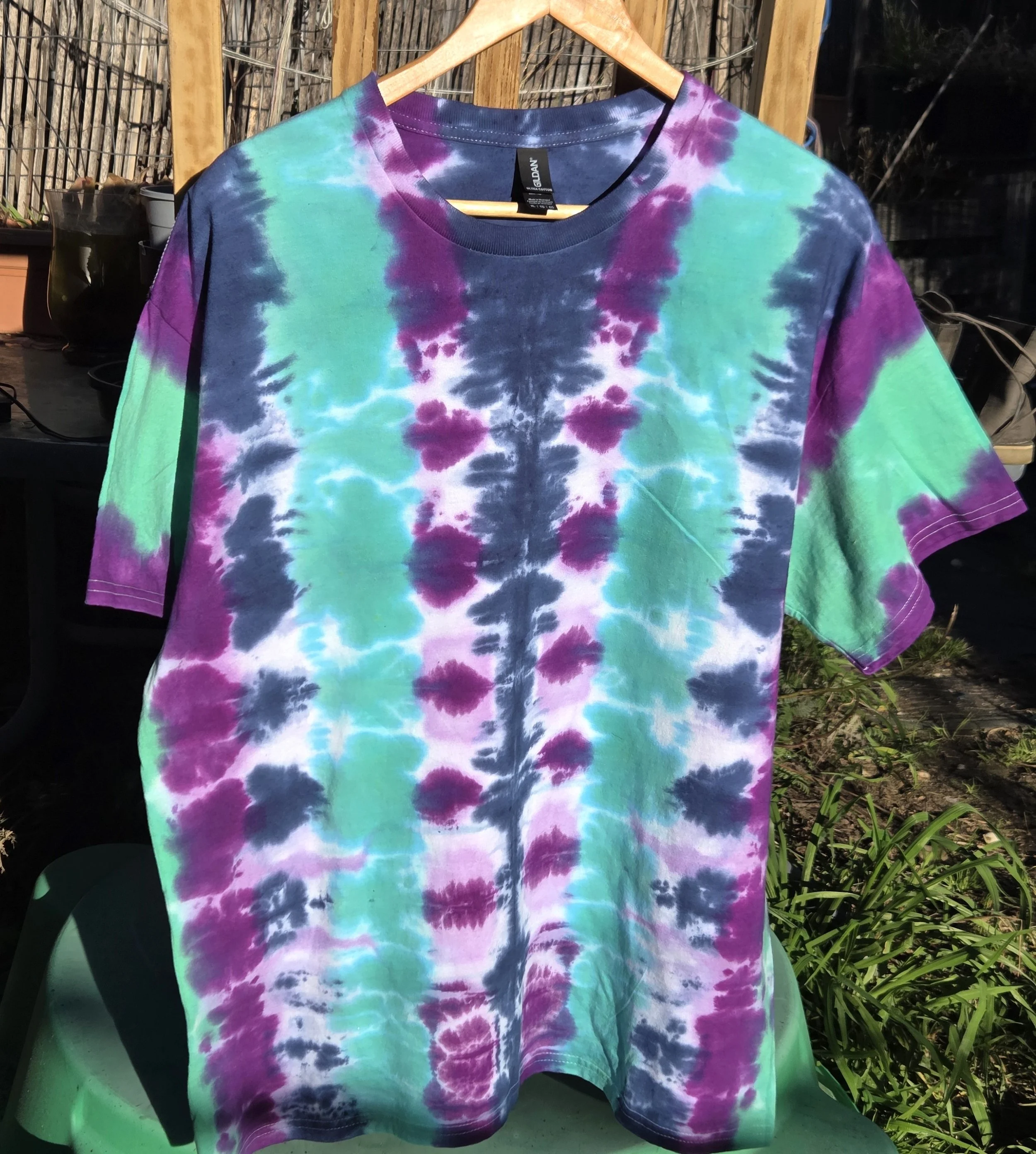 An adult size XL cotton t-shirt featuring vertical tie-dye columns in dark blue, purple, soft lilac, and solid teal green.