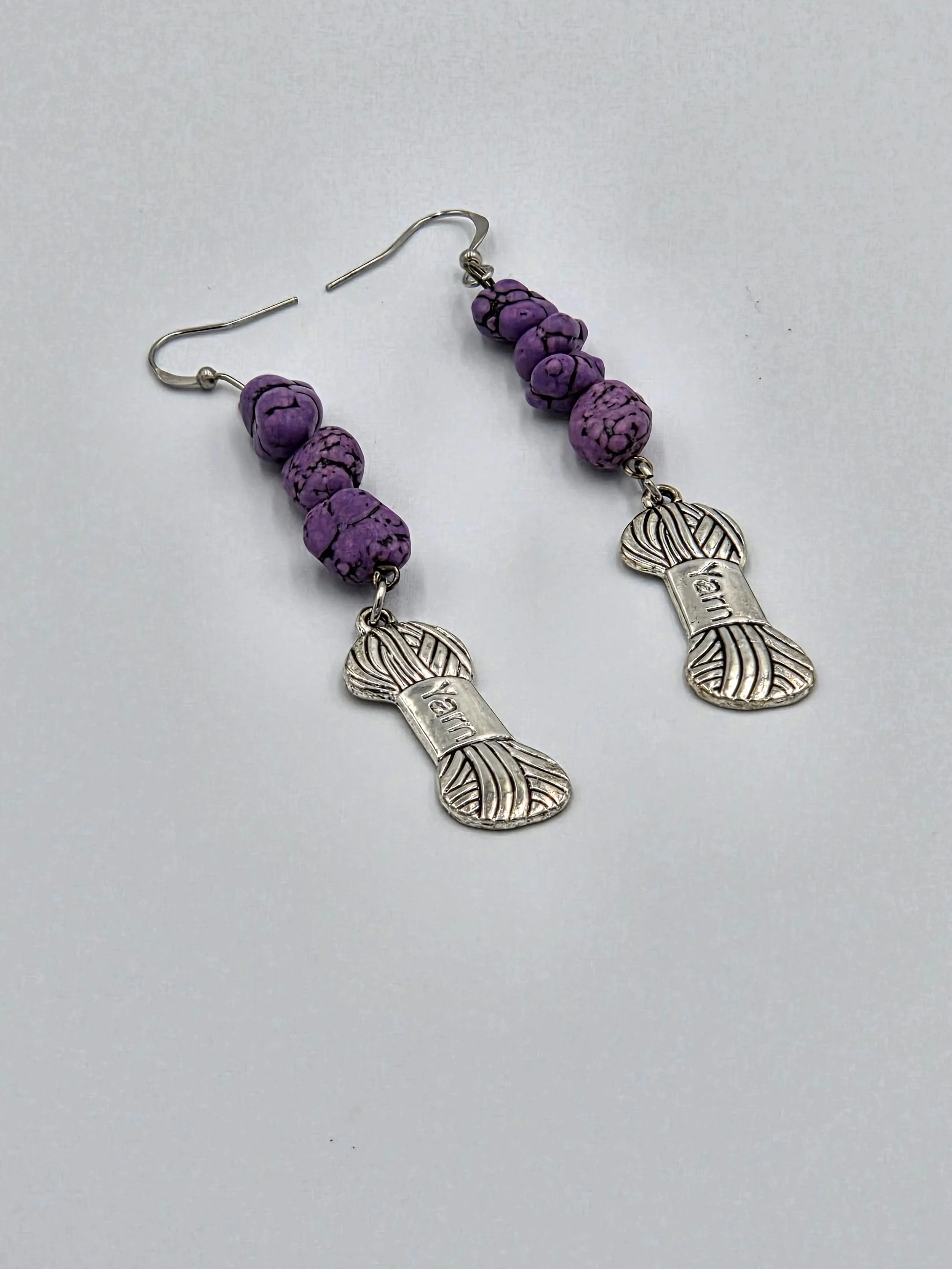 Long silver earrings with purple stone nuggets and a silver yarn charm on silver hooks.
