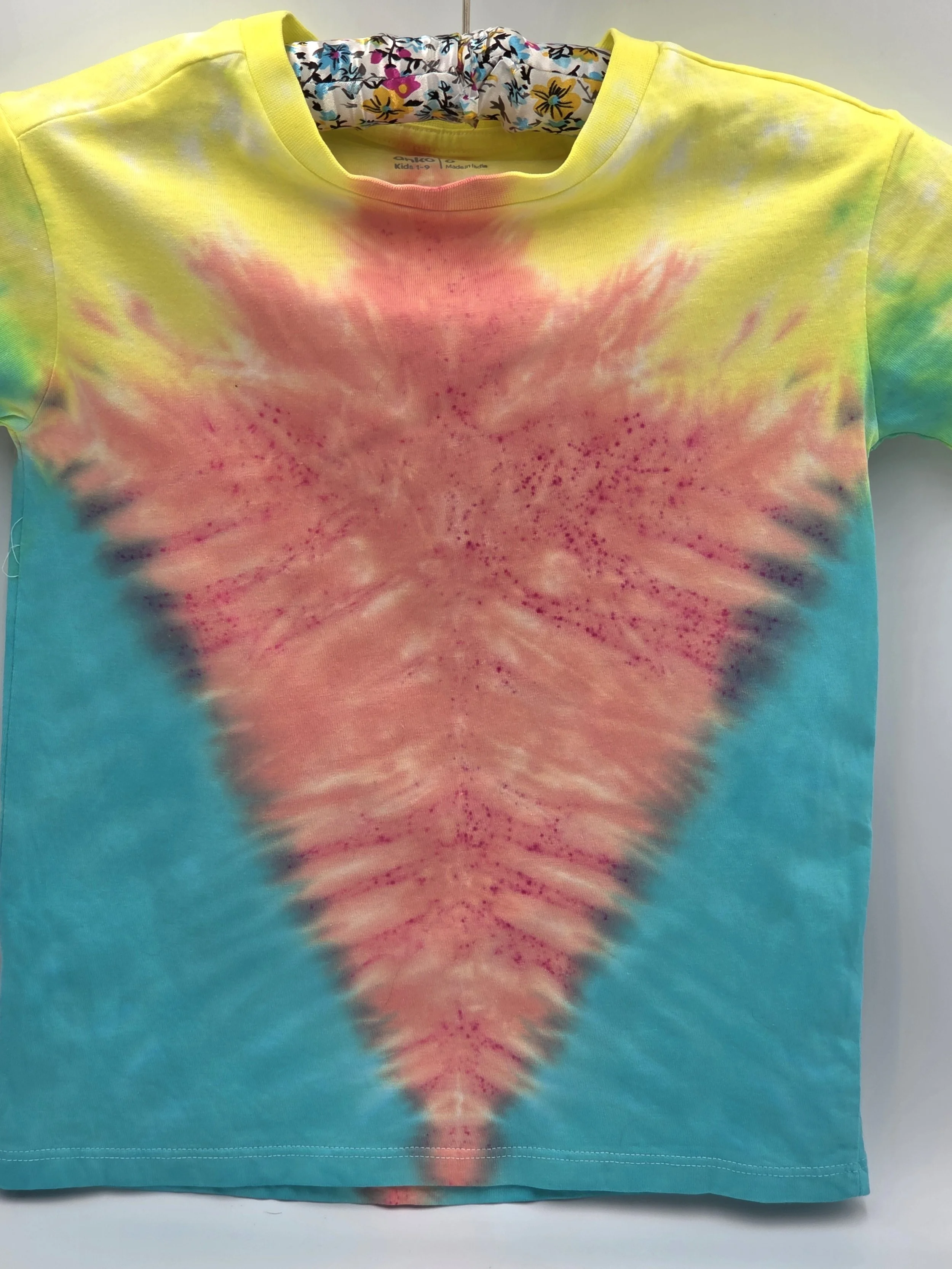 close up of A child's size 6 t-shirt with a half Y-fold tie-dye pattern featuring a central coral V-shape framed by teal sides and yellow shoulders.