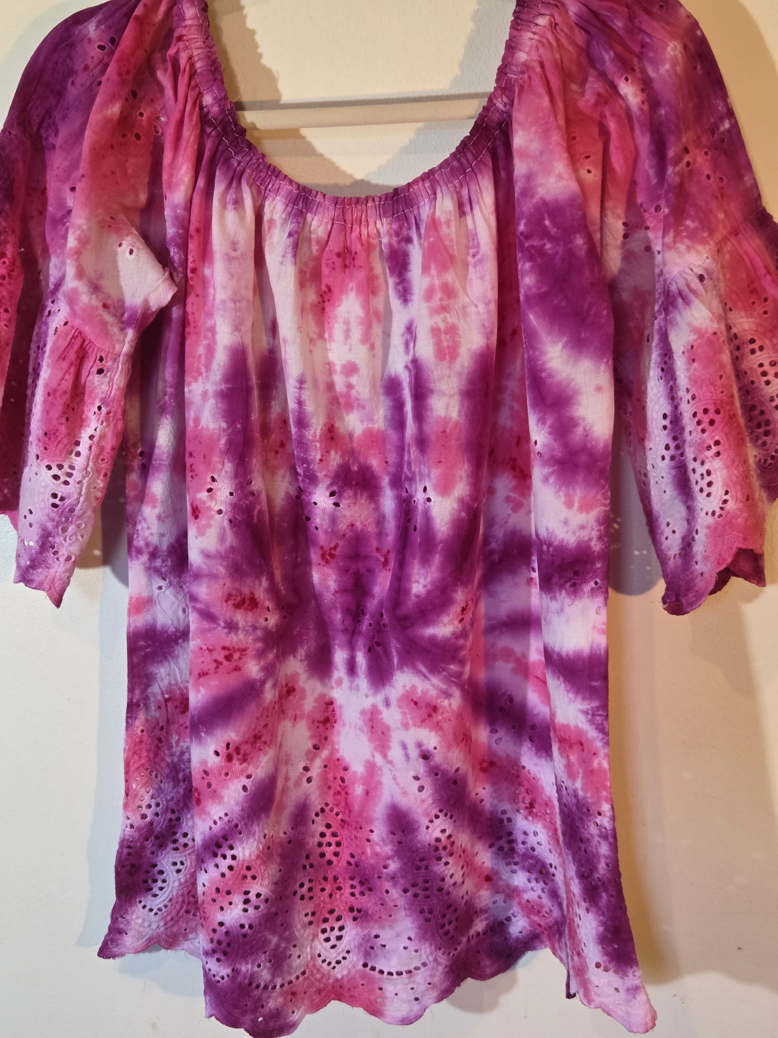 A woman's large white lace bohemian top with bell sleeves, featuring a vivid hand-dyed fuchsia and pink spider flower pattern.