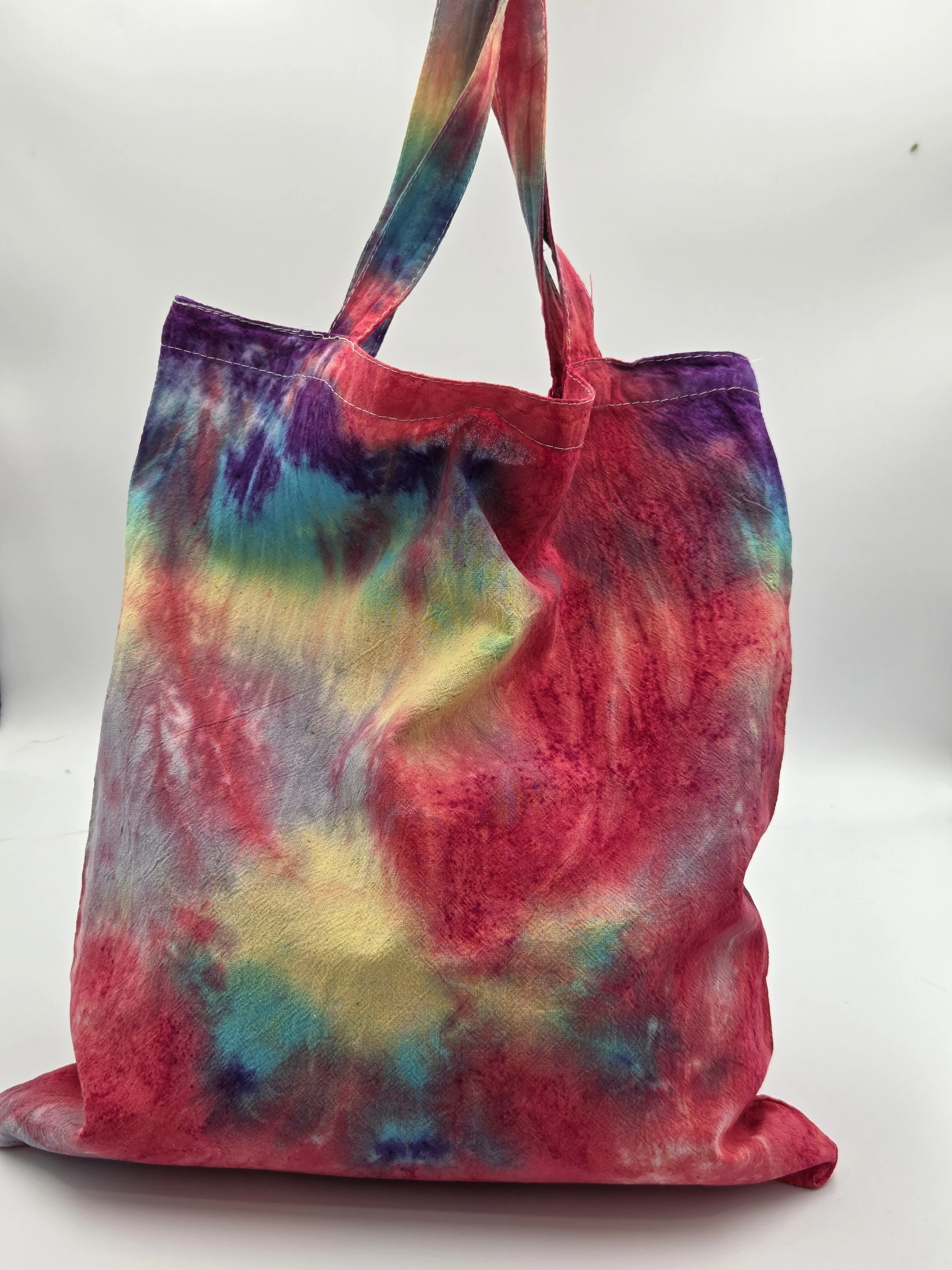 back view A calico tote bag featuring an adaptive tie-dye pattern in coral red, yellow, teal, green, and purple with a playful crab-inspired central motif.