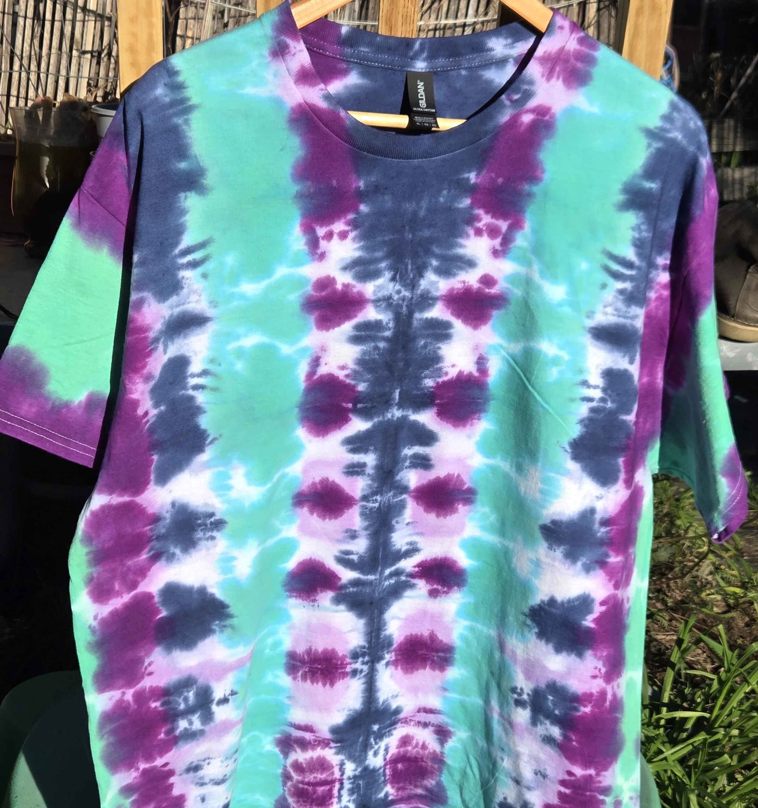 An adult size XL cotton t-shirt featuring vertical tie-dye columns in dark blue, purple, soft lilac, and solid teal green.