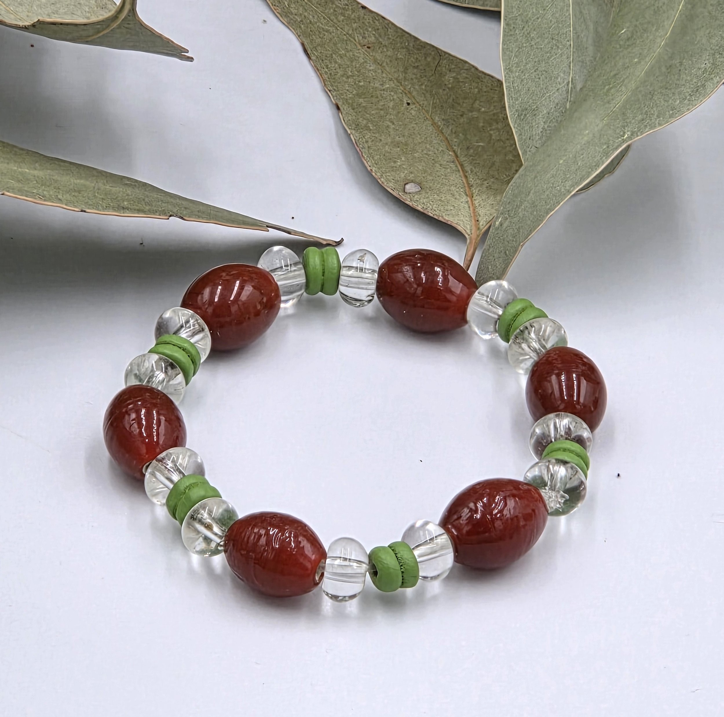 Rust red glass oval beads separated by clear glass donuts and forest green ribbed wood beads on an elastic bracelet.