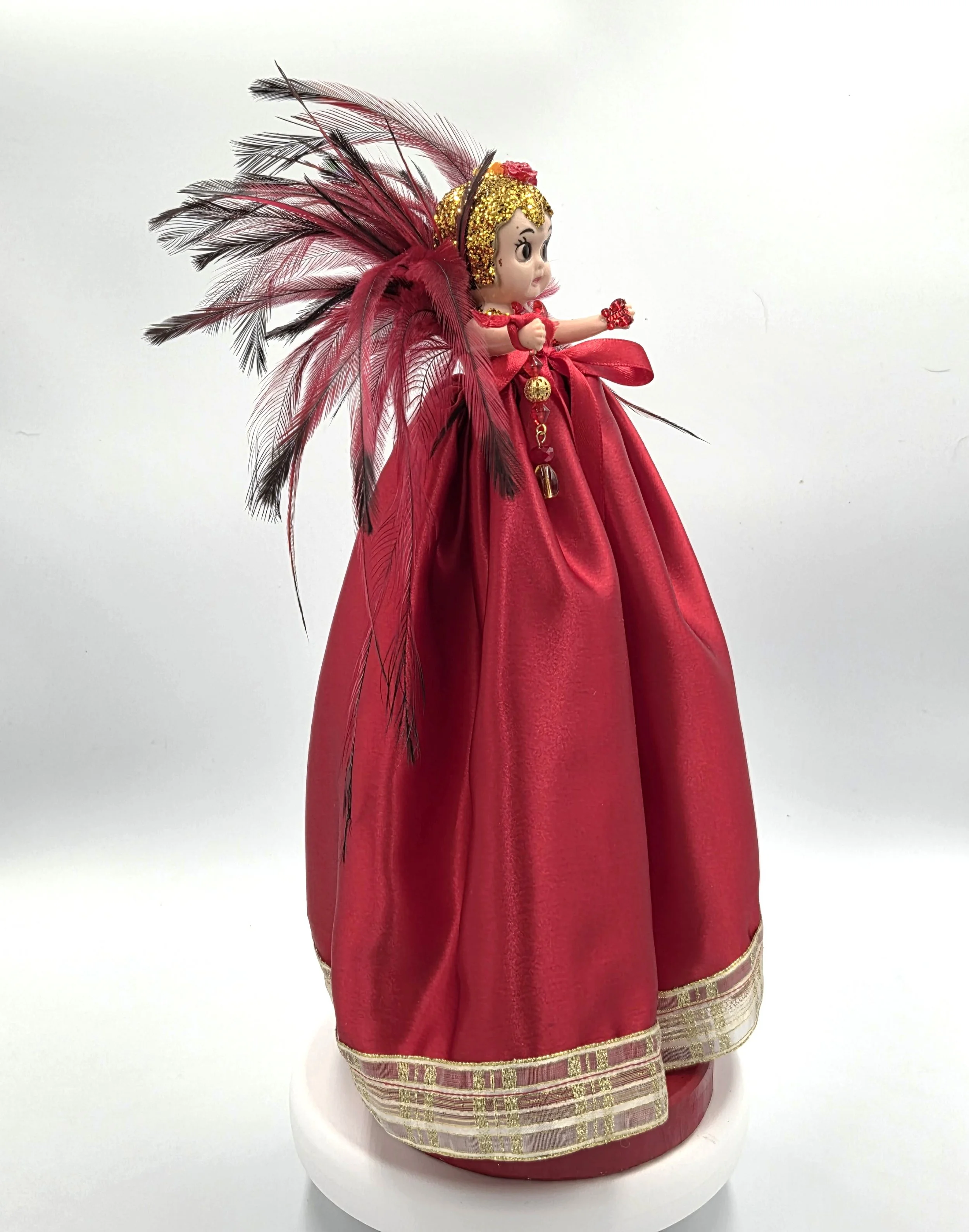 side view OOAK 33cm red satin art doll with a dramatic red and black feather backdrop on a red wooden stand.