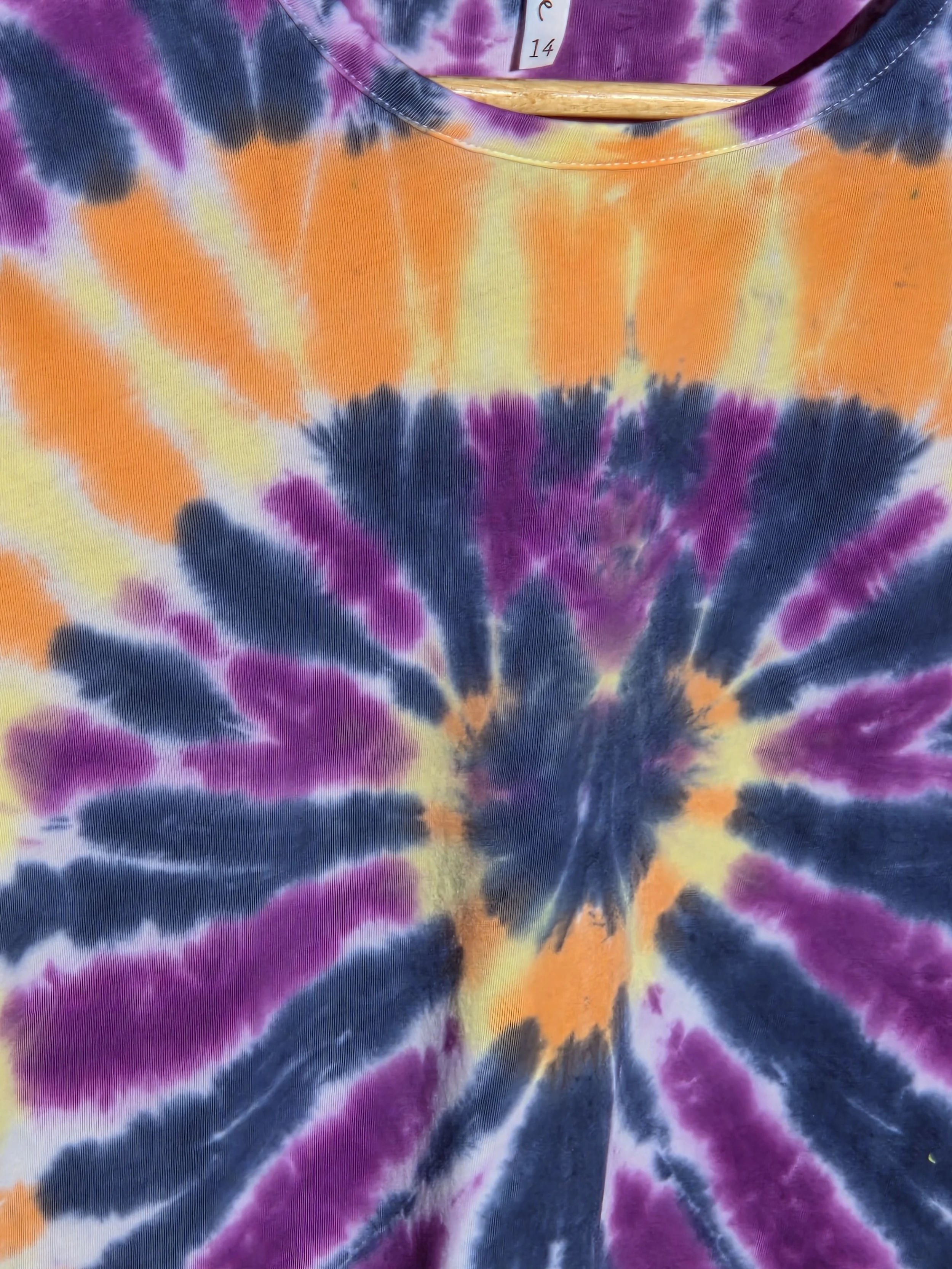 An adult size 14 women's cotton t-shirt featuring a tie-dye sunburst design in purple, dark blue, yellow, and orange.