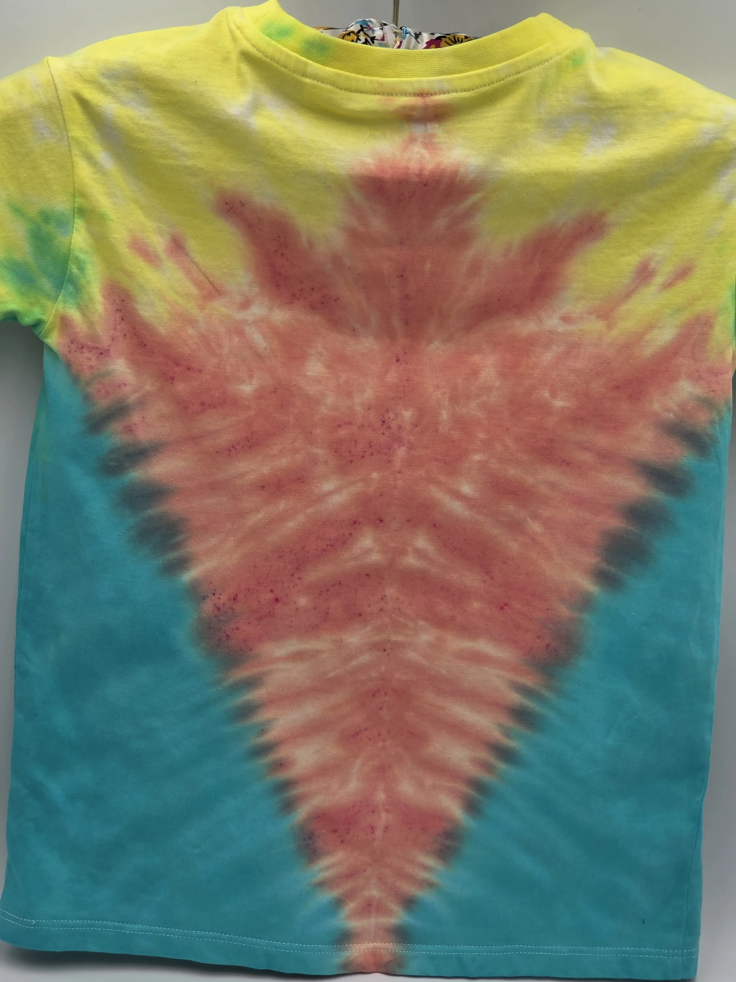 A child's size 6 t-shirt with a half Y-fold tie-dye pattern featuring a central coral V-shape framed by teal sides and yellow shoulders.