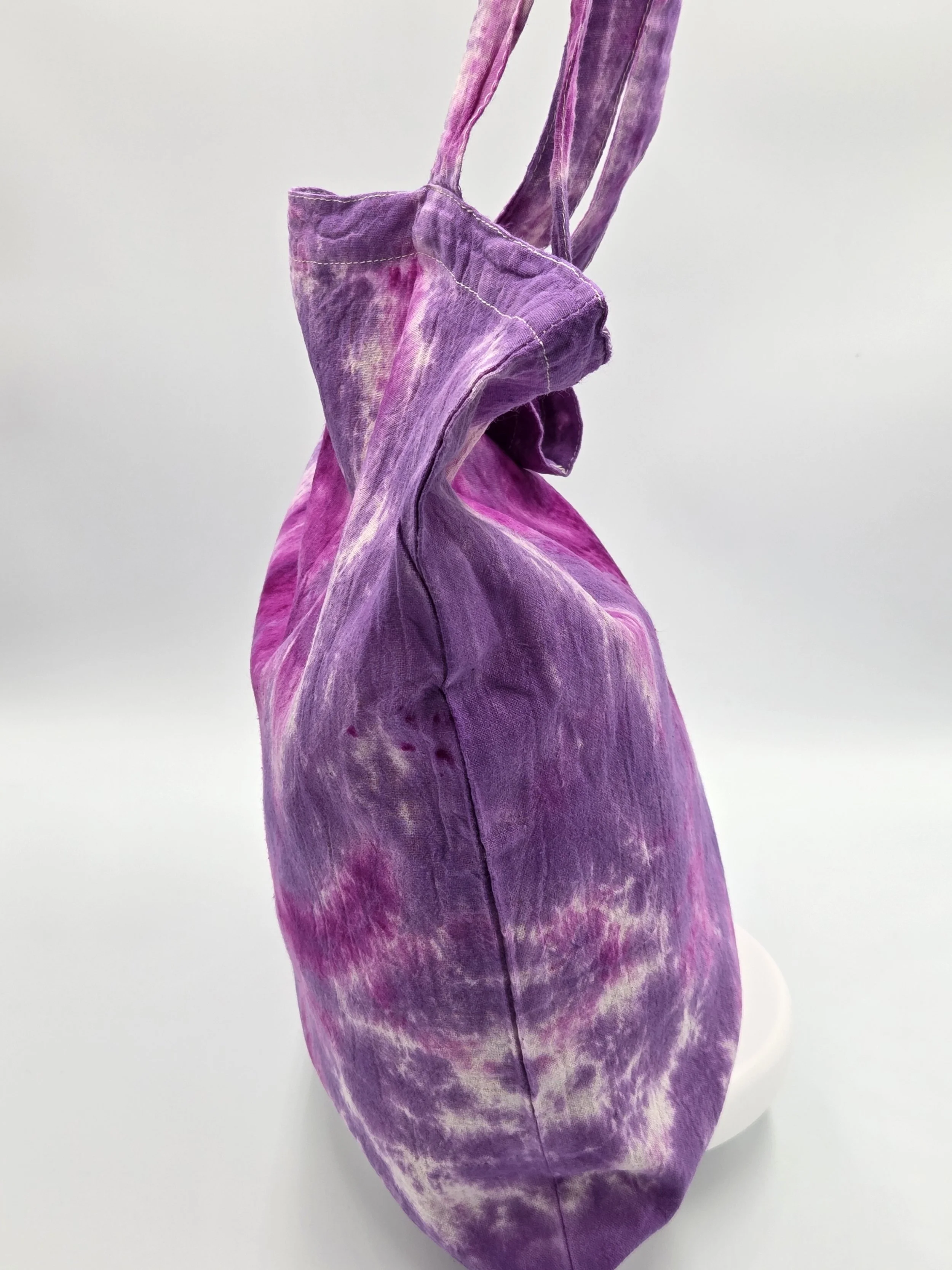 A calico tote bag featuring a tie-dye lotus flower pattern in deep fuchsia resting against a rich purple and white background.