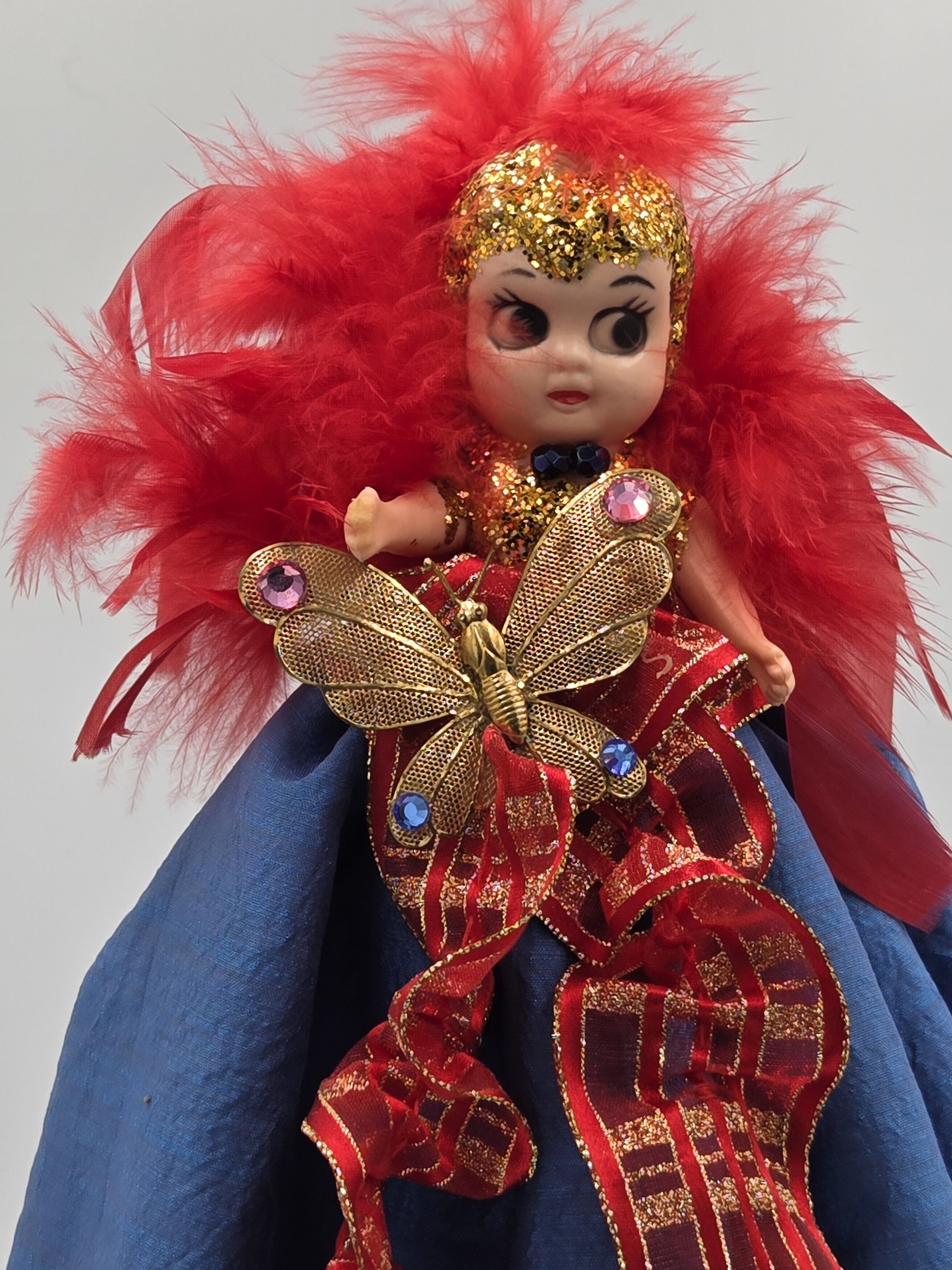 Gold glitter head with black bead choker and red feather framing.