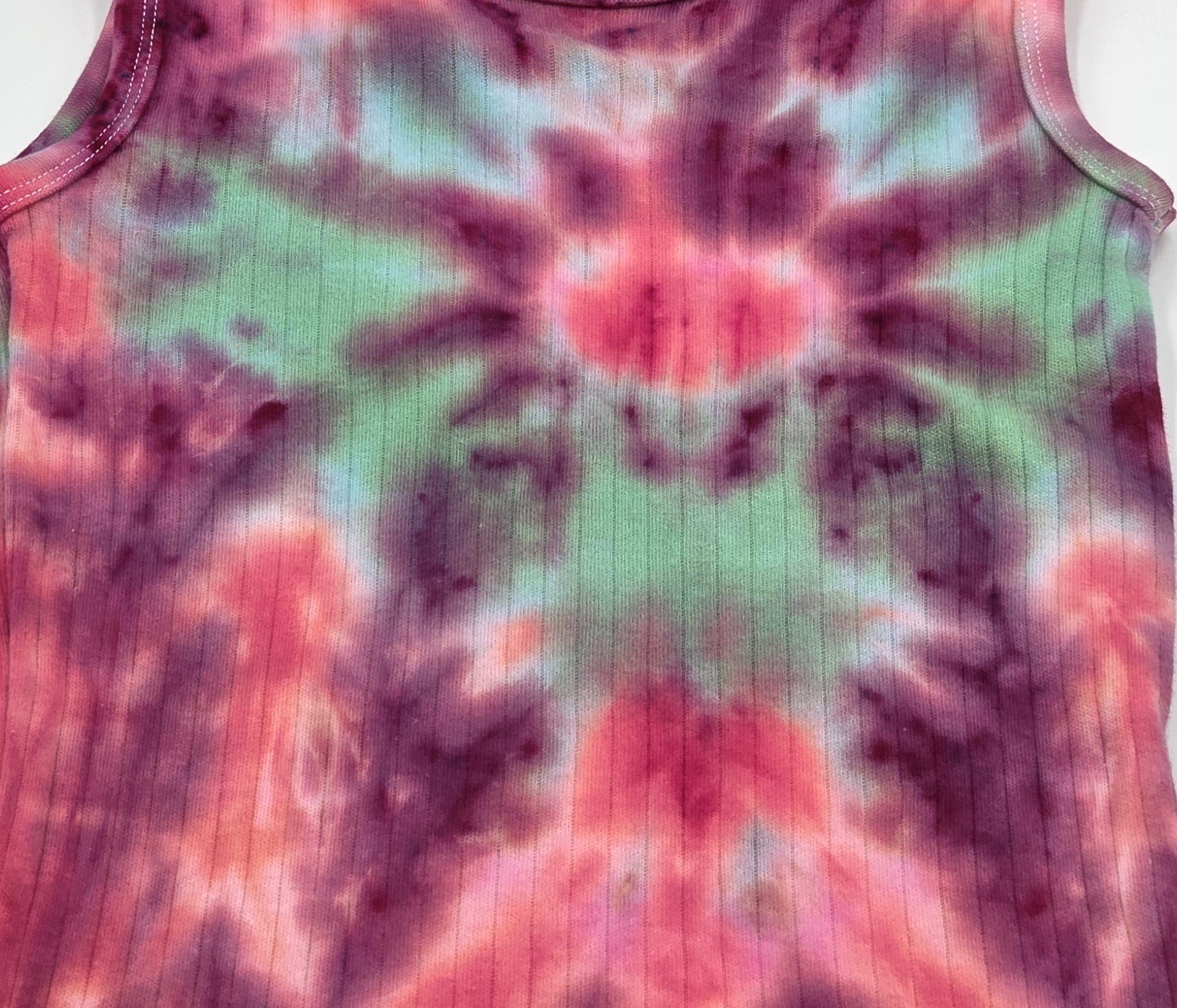 CLOSE UP OF A child's ribbed singlet with a deep burgundy and red tie-dye background, featuring a central green and blue spider pattern that radiates outward.