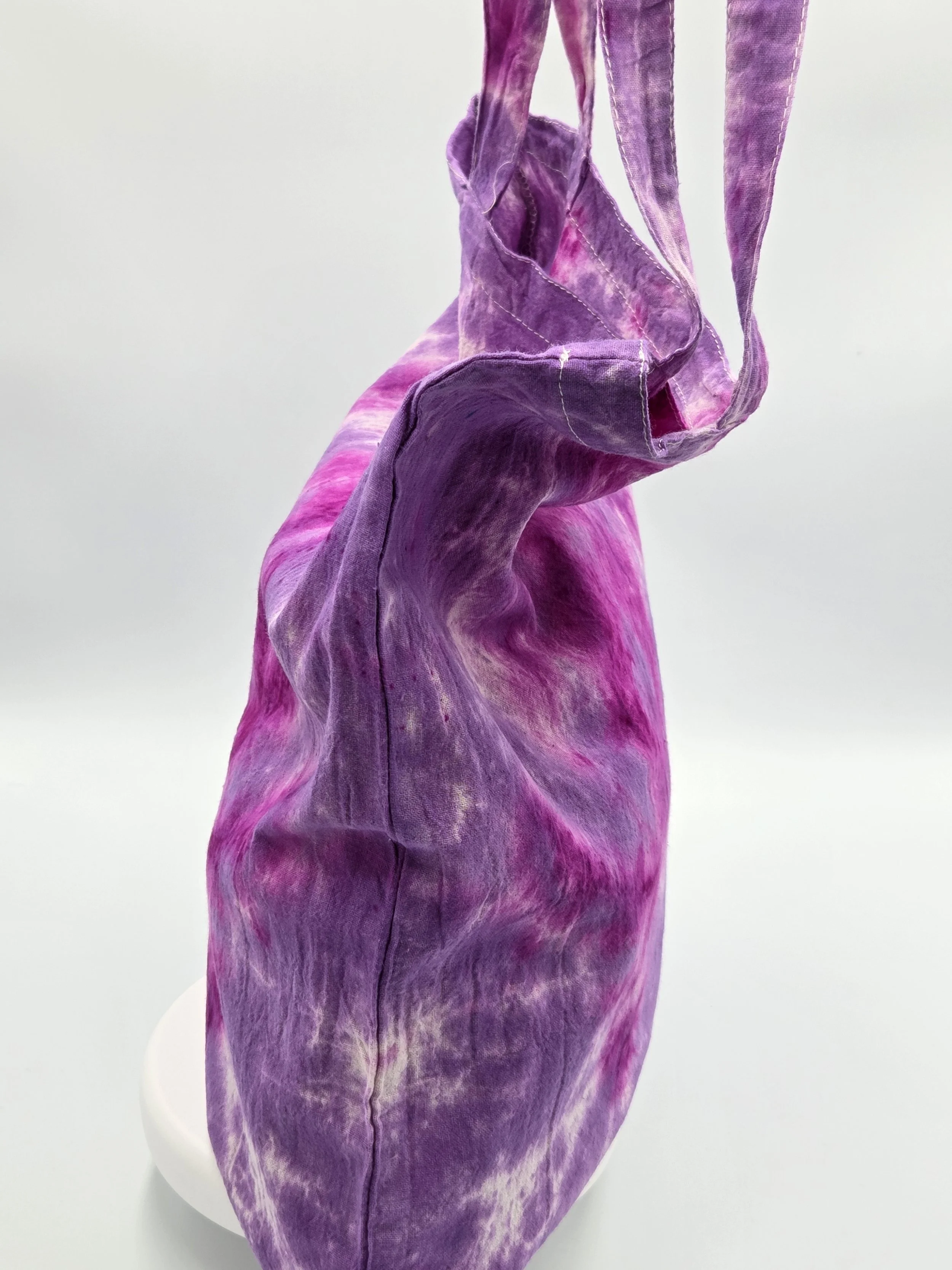 A calico tote bag featuring a tie-dye lotus flower pattern in deep fuchsia resting against a rich purple and white background.