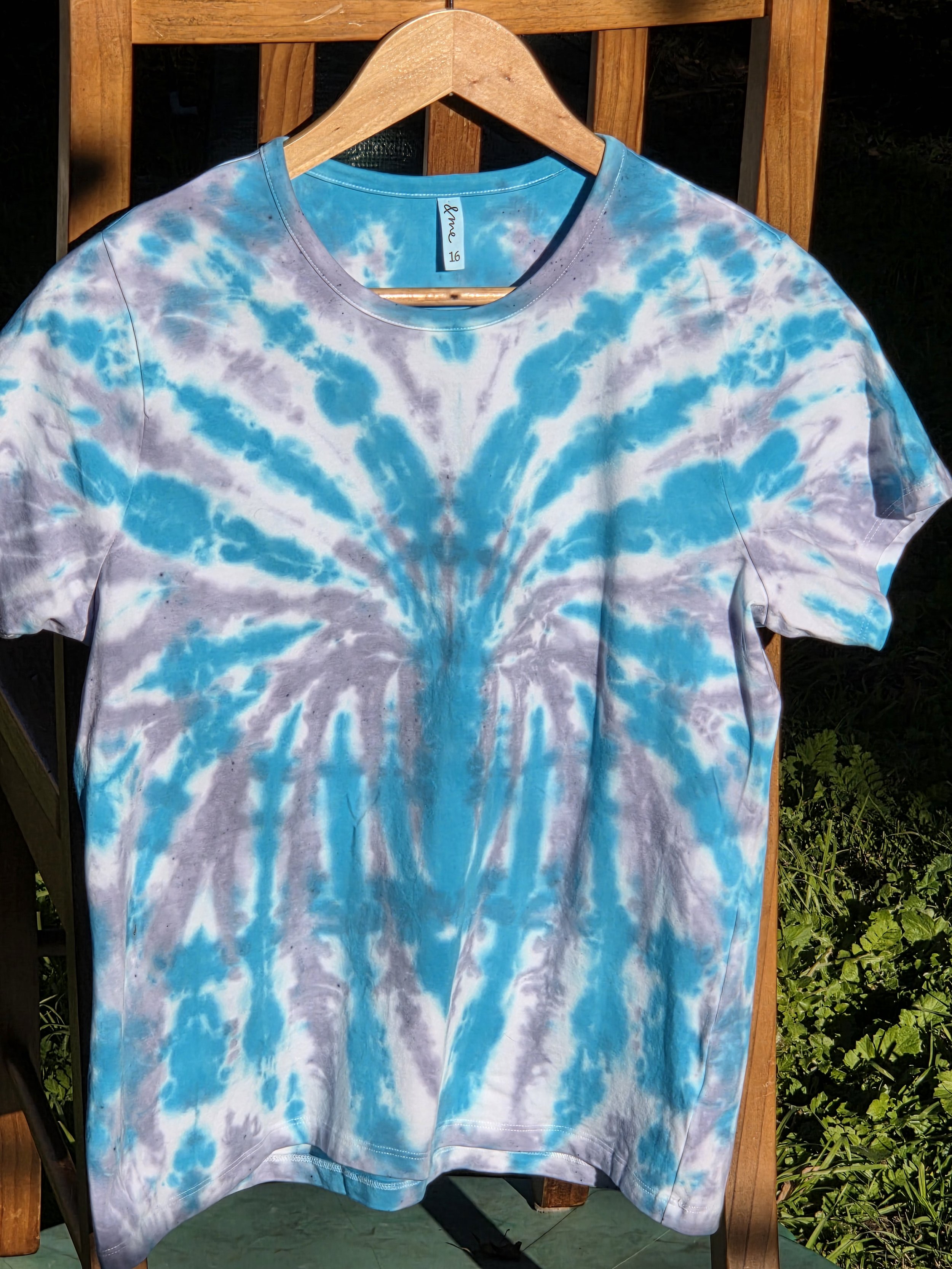 A size 16 t-shirt featuring a highly defined tie-dye spider pattern in bright aquamarine against a soft grey and white background.