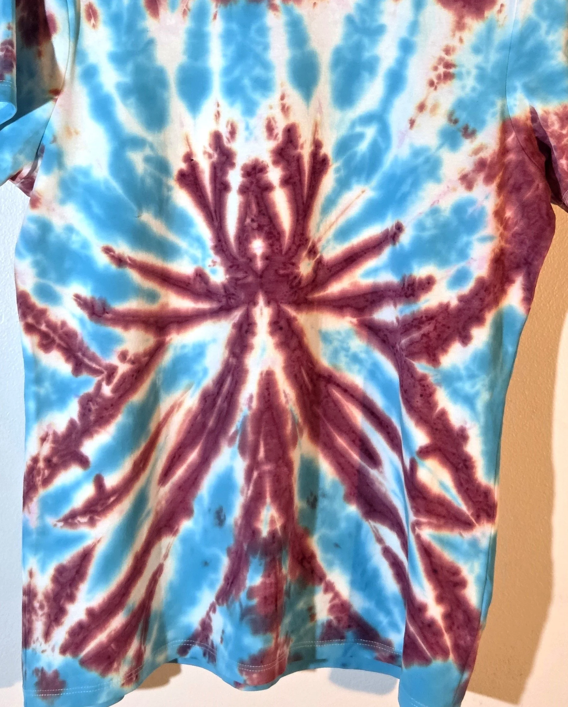 A size 10 t-shirt featuring a tie-dye pattern of a sharp, spiky purple and wine flower on a sky blue and white background.