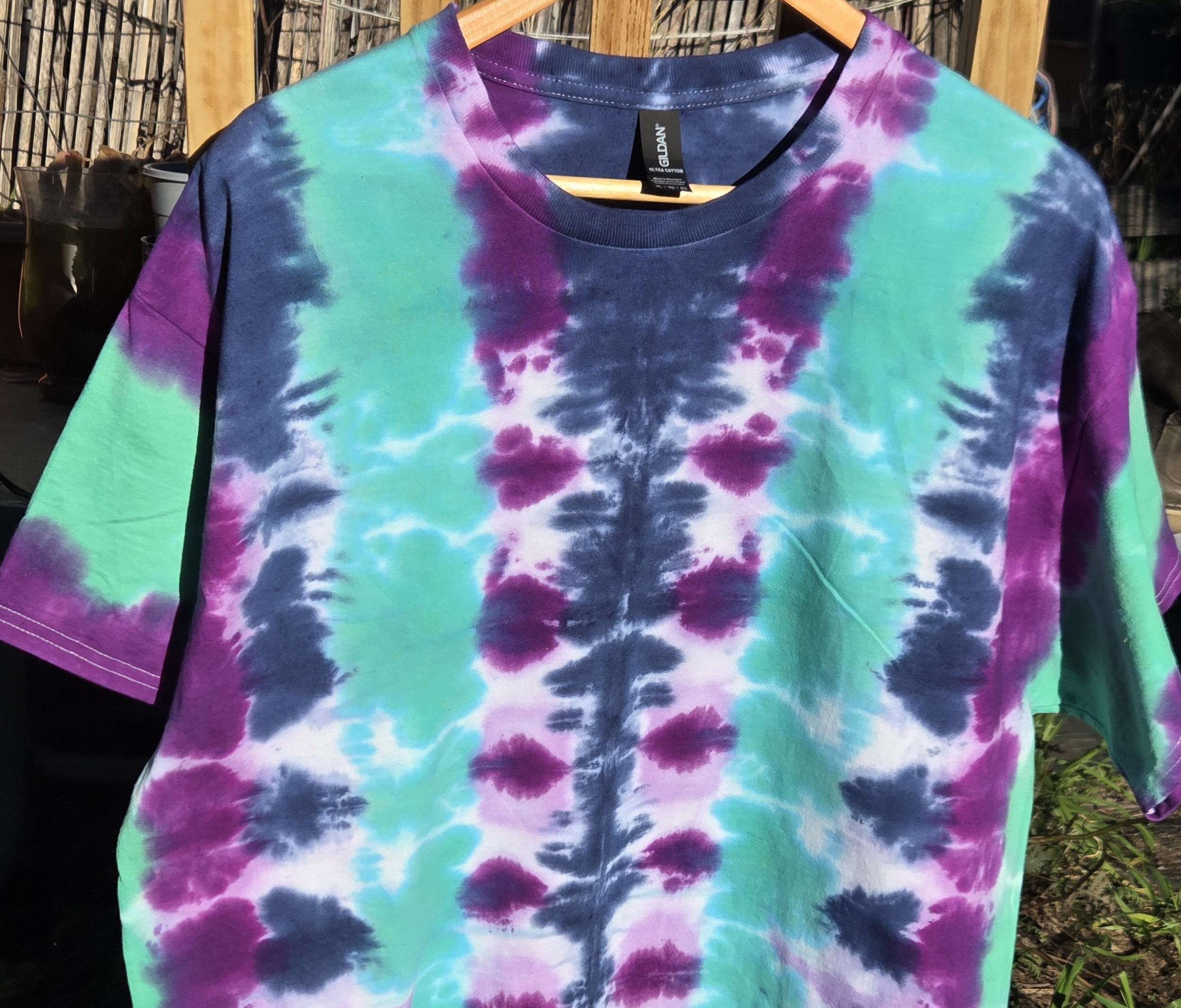 An adult size XL cotton t-shirt featuring vertical tie-dye columns in dark blue, purple, soft lilac, and solid teal green.
