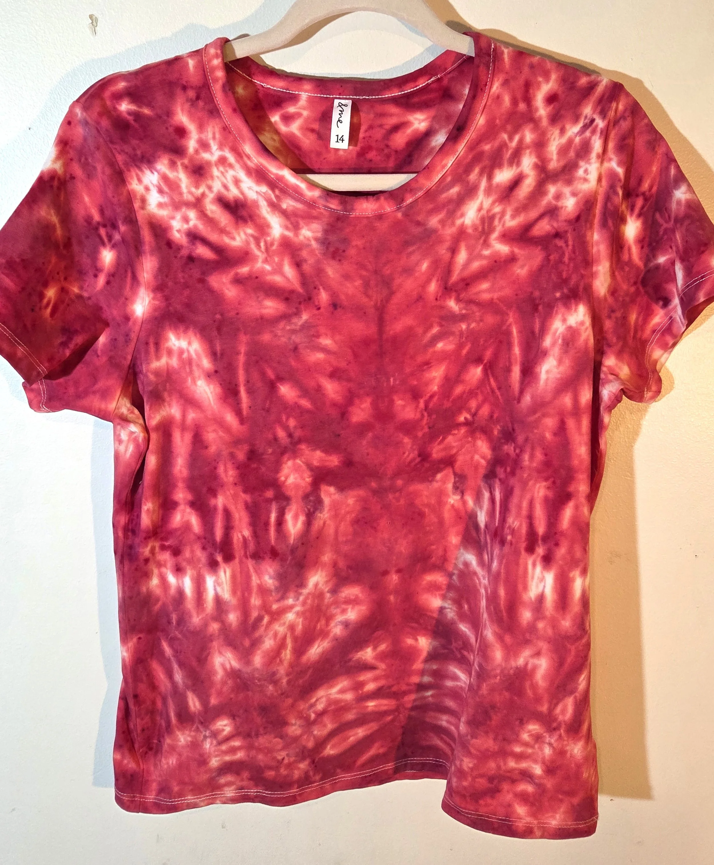 A size 14 women's t-shirt featuring a highly saturated red and coral tie-dye pattern of abstract swirls radiating from the center.