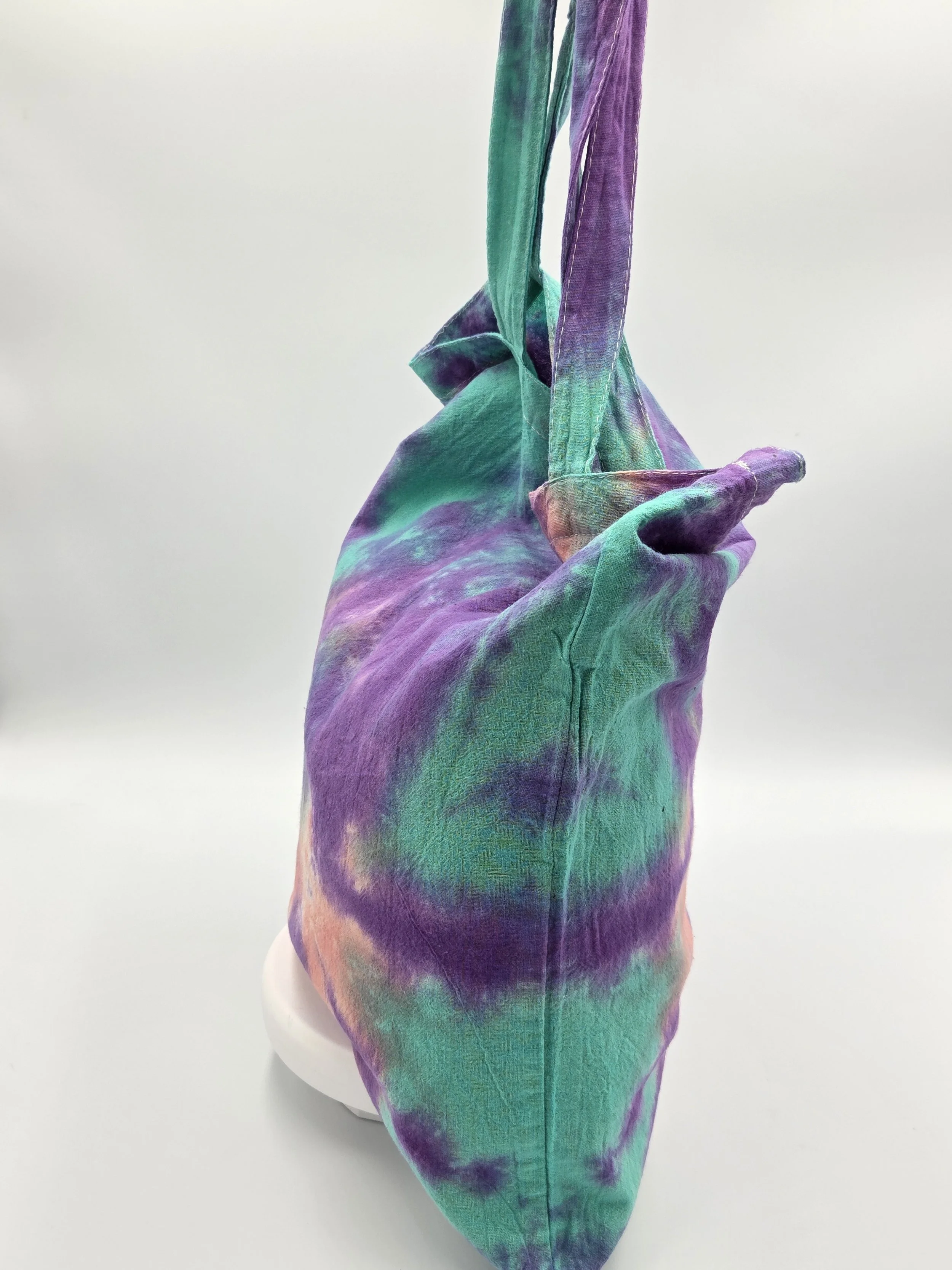 A calico tote bag featuring a tie-dye sea anemone pattern with a coral body and purple arms against a bright teal background.