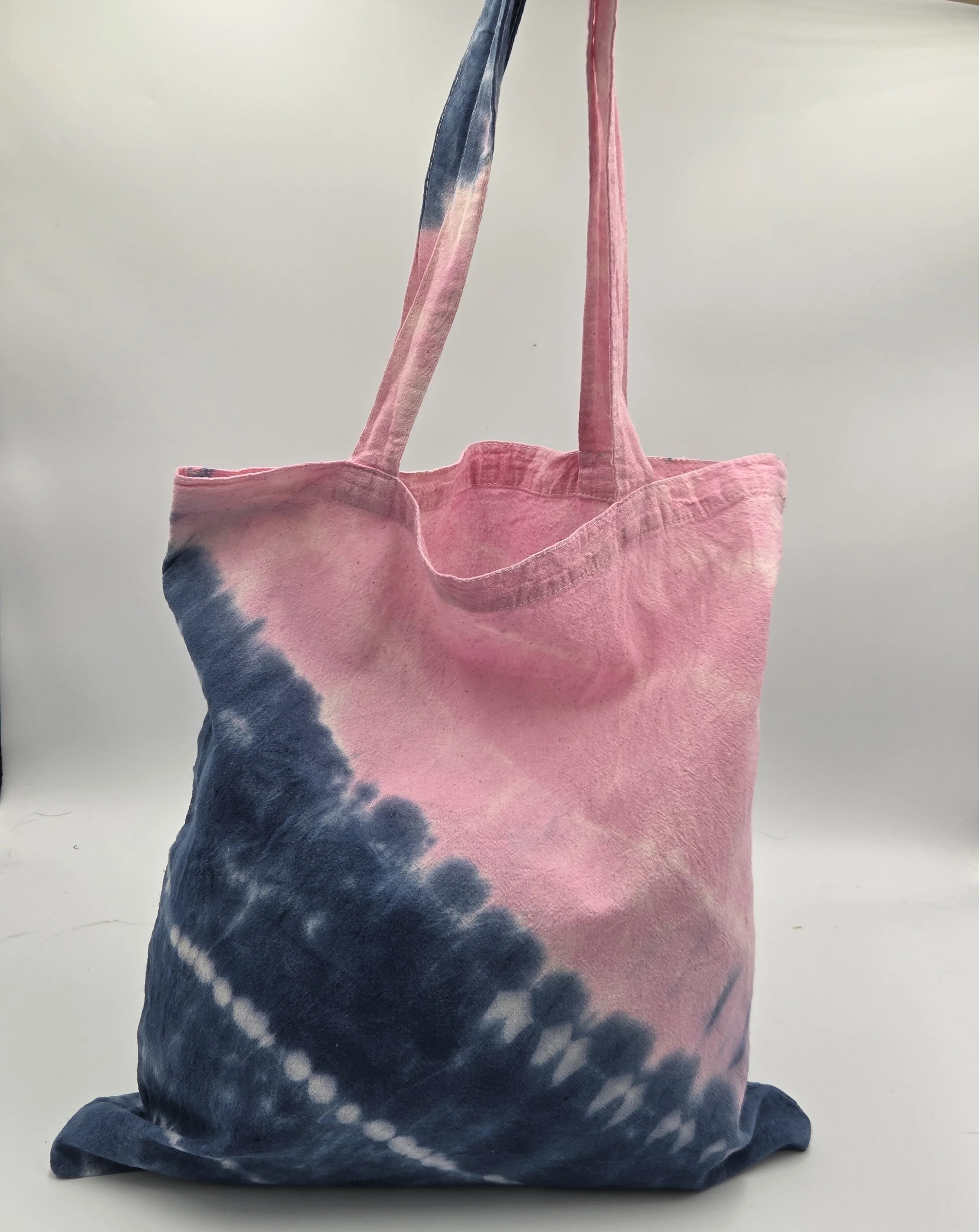 calico tote bag with a diagonal tie-dye split featuring pink on top and dark blue on the bottom with three batik resist lines.