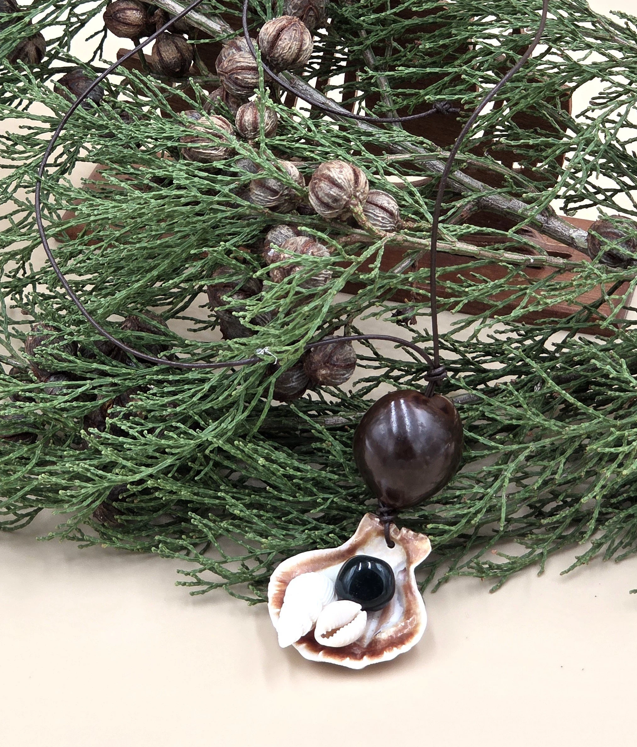 on a background of native pine leaves and nuts  handmade necklace with clam shell collage and seed pod on leather cord. OOAK