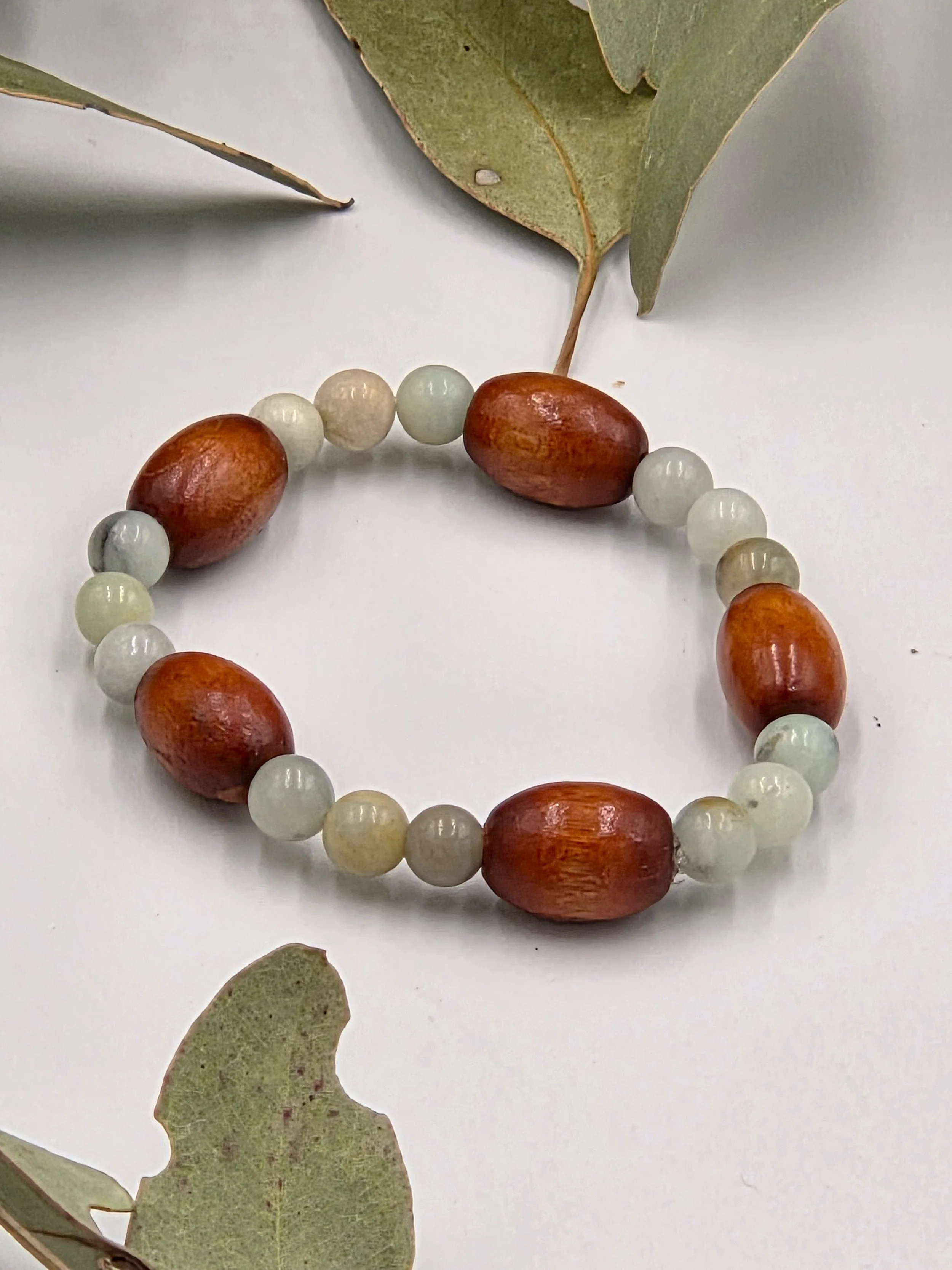Smooth green Amazonite beads alternating in sets of three with single large brown oval wood beads on an elastic bracelet.