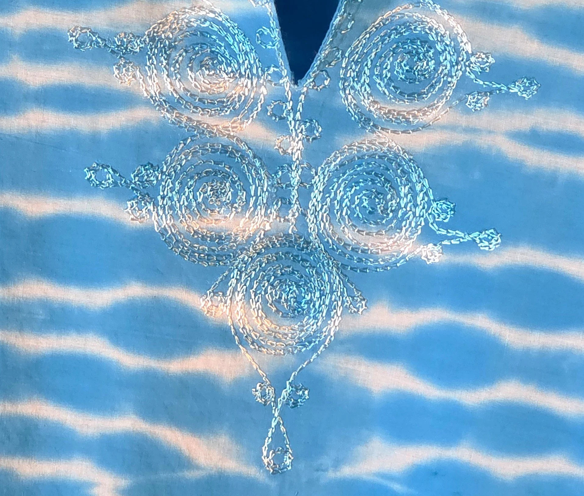 embriodered details of A light blue cotton kaftan shirt with embroidered details, showcasing a vertical tie-dye pattern of thin, wire-like white ripple lines.