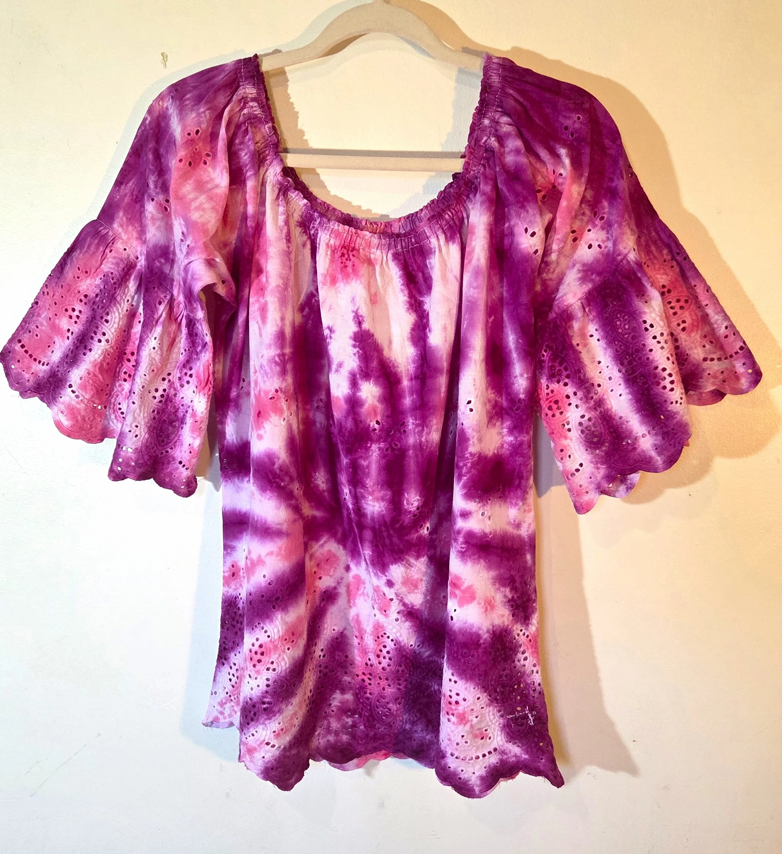 A woman's large white lace bohemian top with bell sleeves, featuring a vivid hand-dyed fuchsia and pink spider flower pattern.