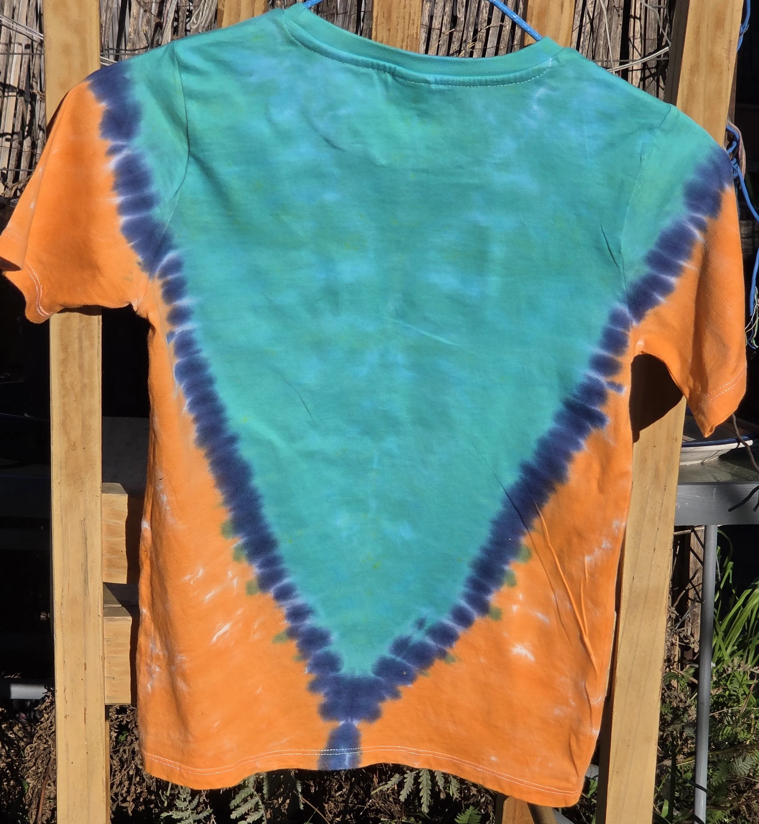 A child size 7 cotton t-shirt featuring a large teal and dark blue V-shape tie-dye pattern against a bright orange background.