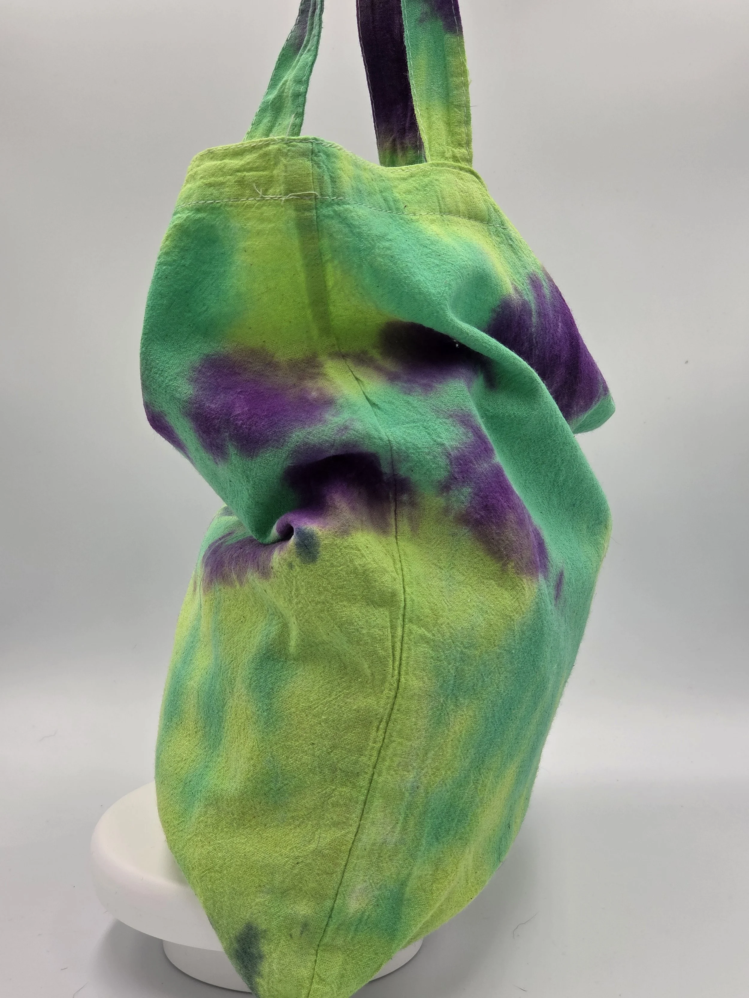 A calico tote bag featuring an abstract dark blue and purple half-circle tie-dye pattern against a lime green and pastel yellow background.