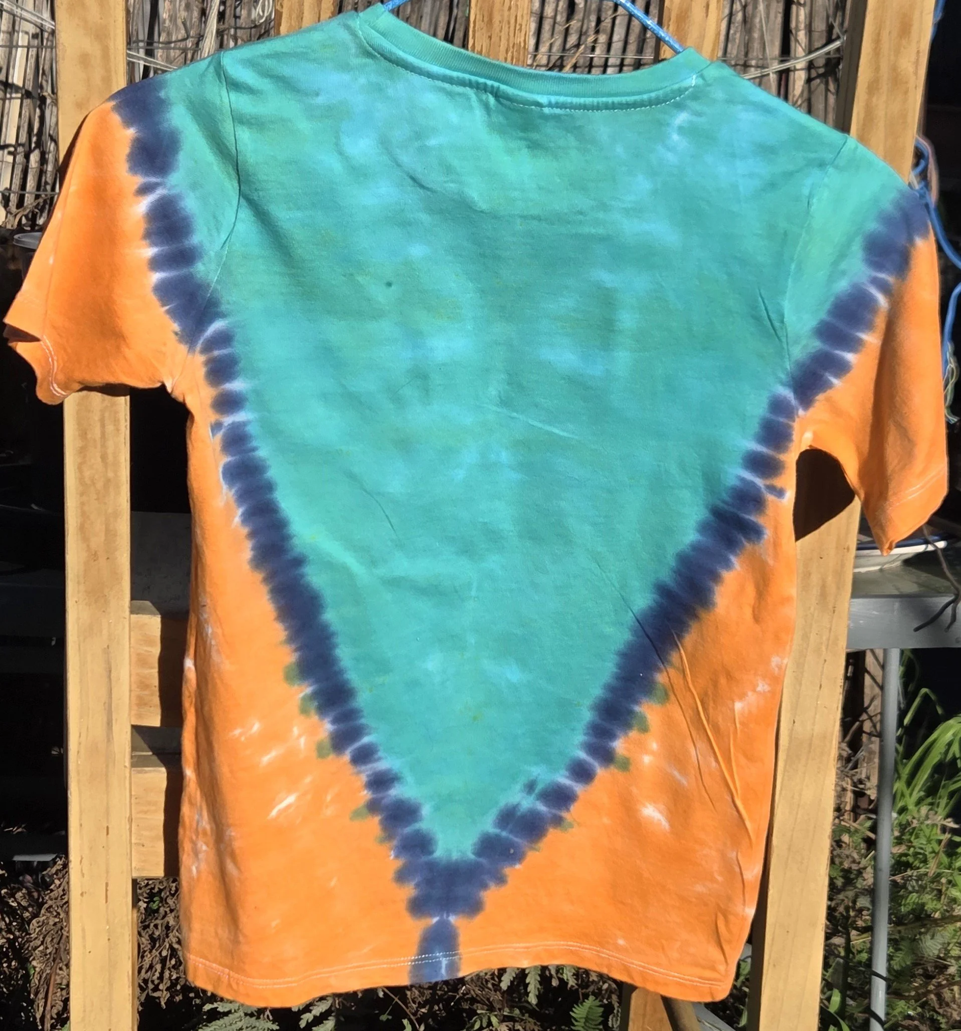 A child size 7 cotton t-shirt featuring a large teal and dark blue V-shape tie-dye pattern against a bright orange background.