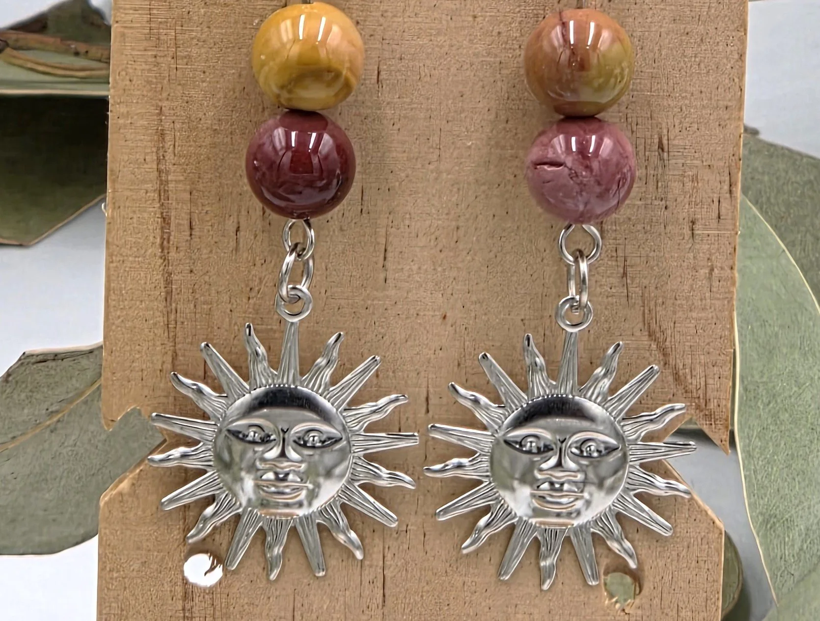 close up of Reddish-brown Mookaite beads with a silver sun face charm on sterling silver dangle earring hooks.
