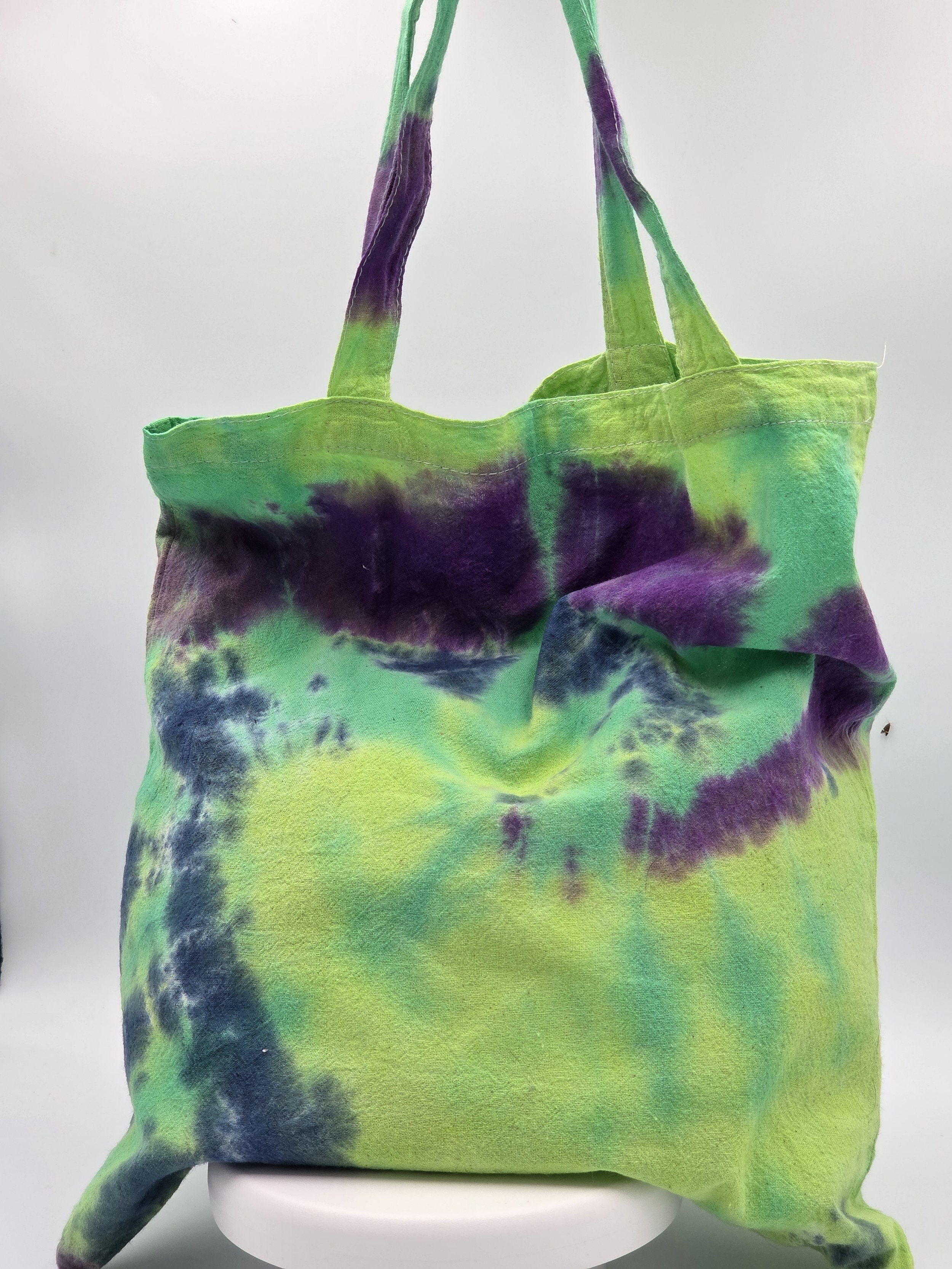 A calico tote bag featuring an abstract dark blue and purple half-circle tie-dye pattern against a lime green and pastel yellow background.
