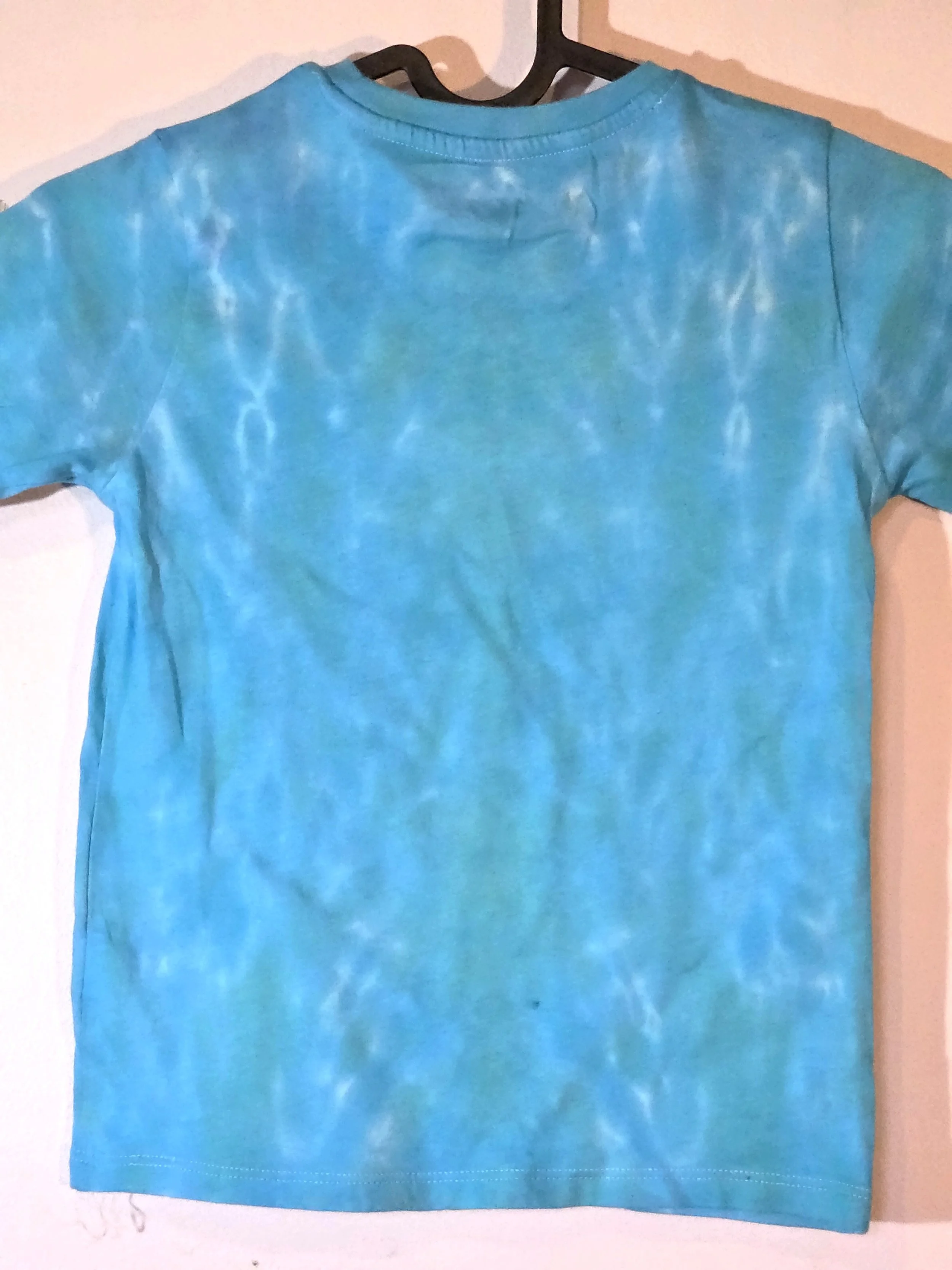 close up of back view A child's sky blue t-shirt displaying a delicate, flowing tiger stripe tie-dye pattern with thin white veins near the shoulders.