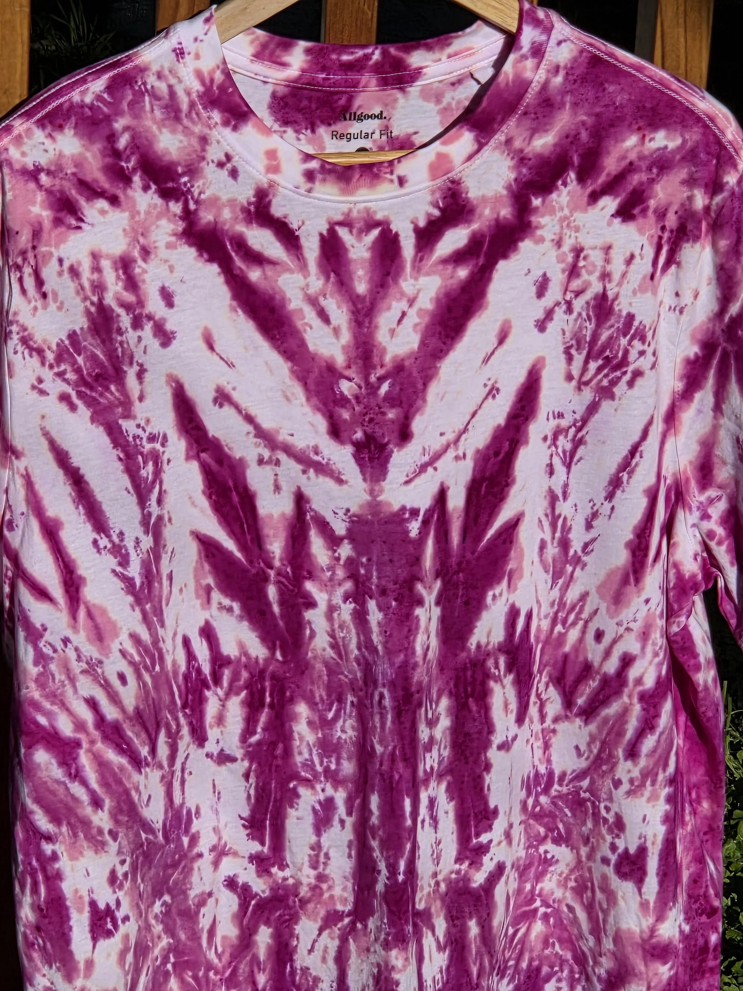 close up of A large adult white t-shirt featuring a tie-dye pattern of a deep wine feathery central motif against an abstract pink background.