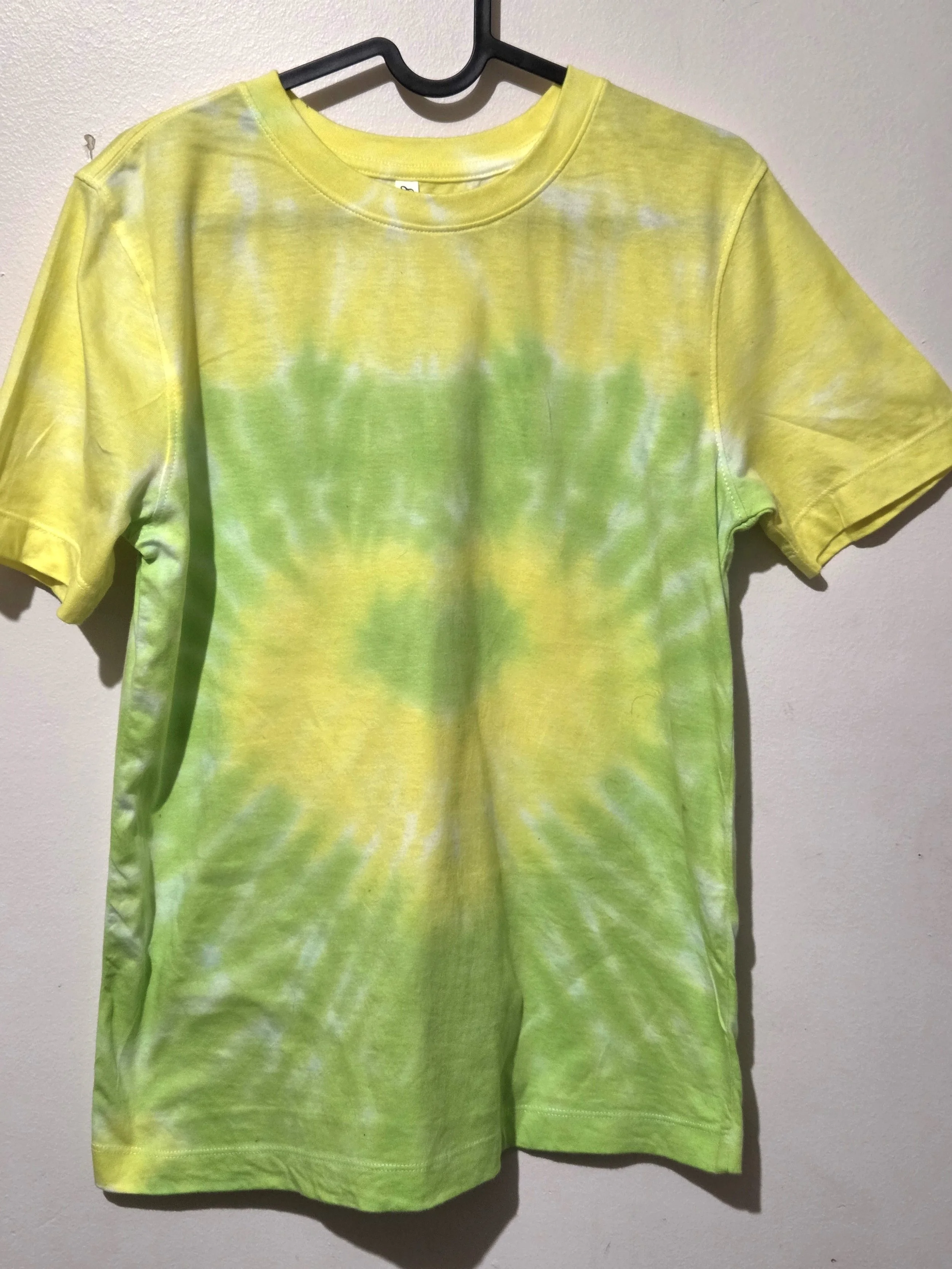 An adult size 10 women's cotton t-shirt featuring a tie-dye heart pattern in subtle pastel yellow and lime green.
