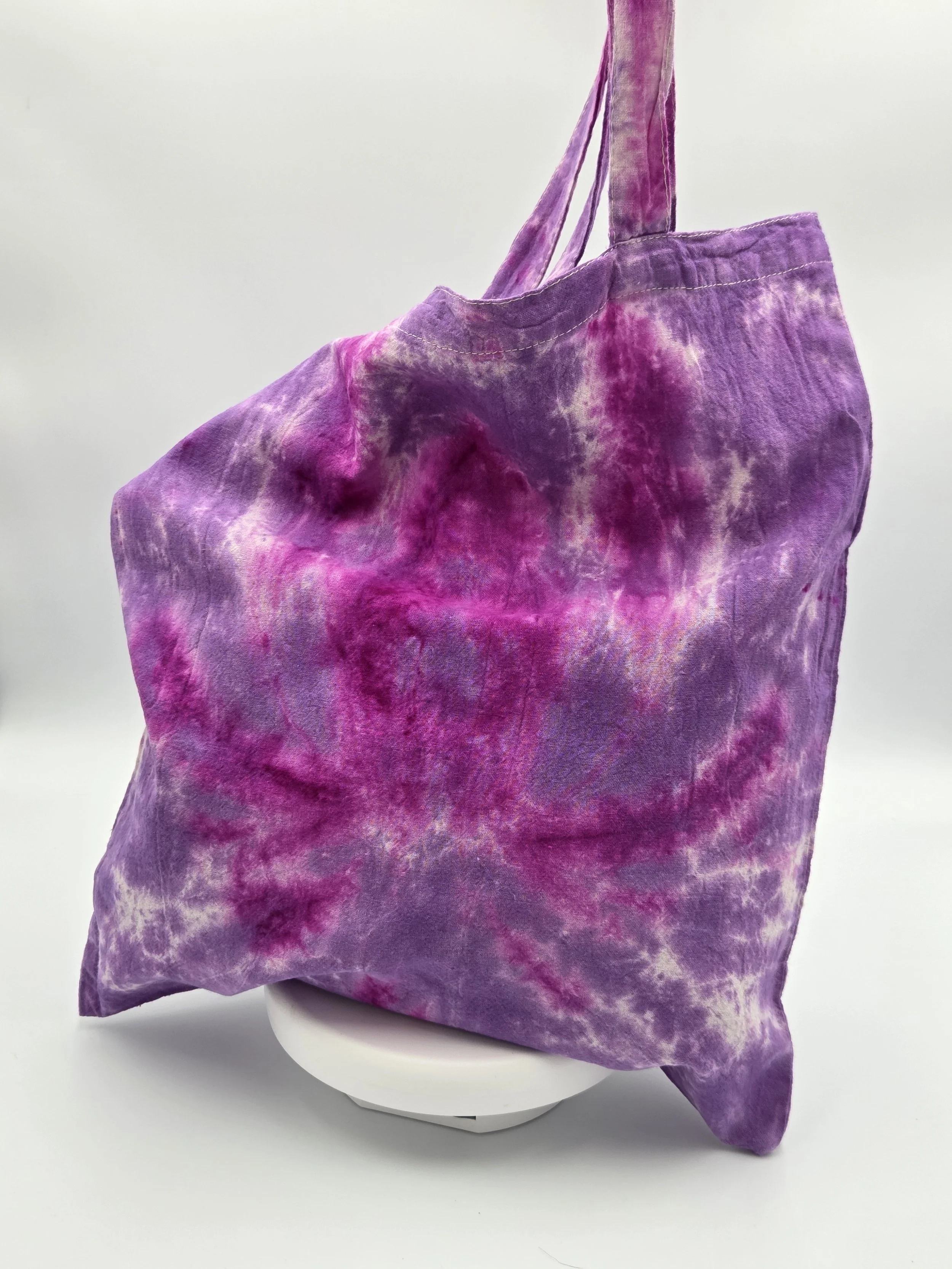 A calico tote bag featuring a tie-dye lotus flower pattern in deep fuchsia resting against a rich purple and white background.